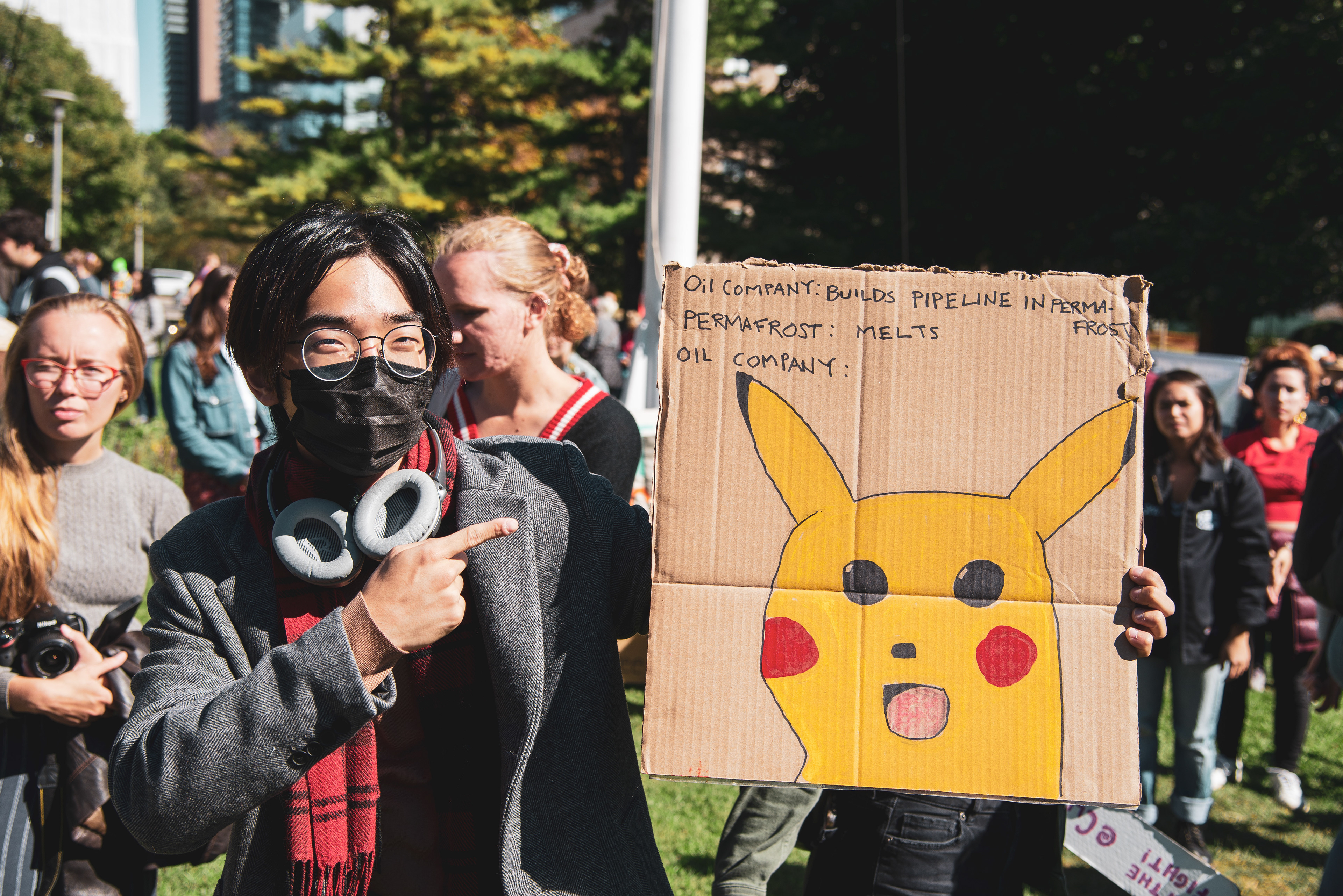 A young man shows off a sign featuring a meme mocking oil companies for building pipelines in permafrost. (Aloysius Wong)