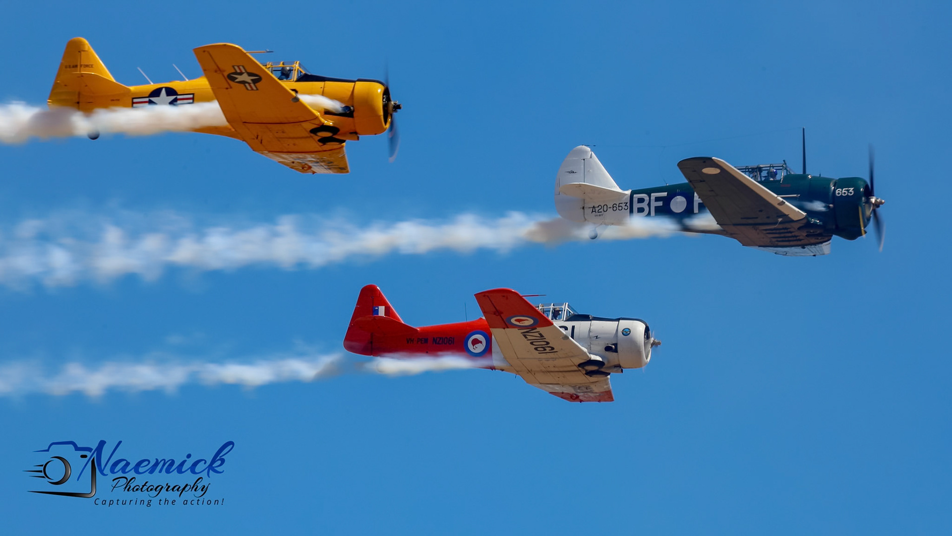 Three vintage airplanes, including North American T-6 Texan aircraft, perform an aerial display with smoke trails in Temora, New South Wales, Australia.
