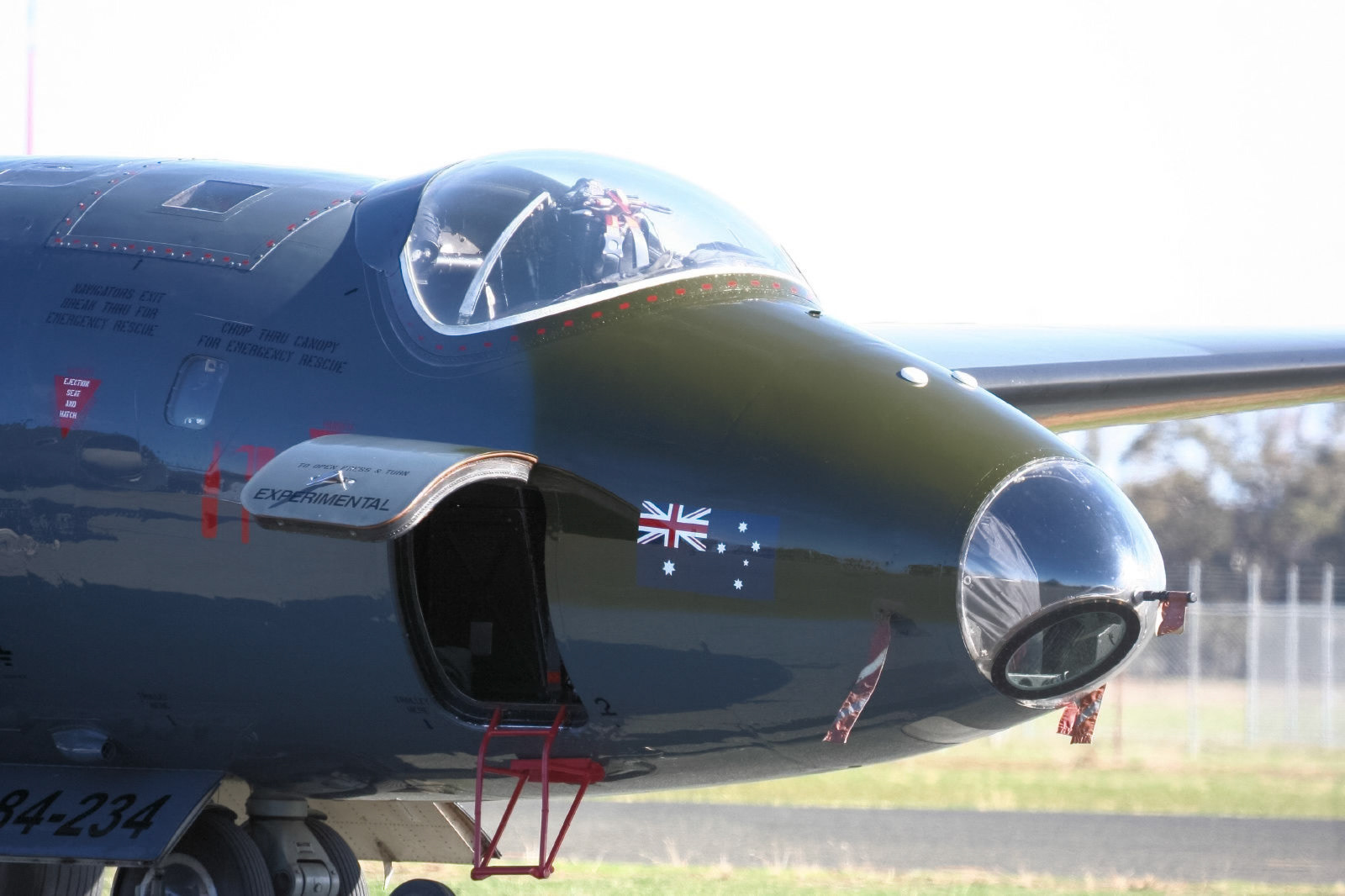 A close-up view of the nose section and cockpit of a dark aircraft, featuring an Australian flag decal and the word "EXPERIMENTAL" visible on its side.