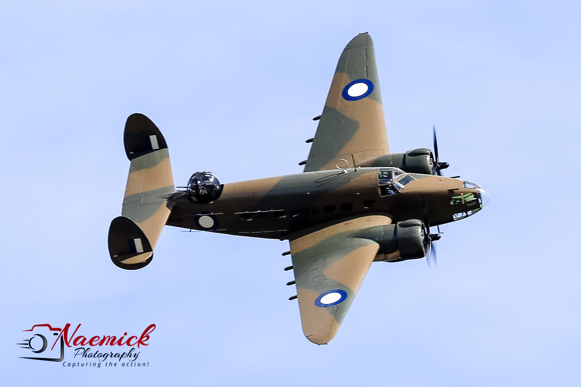 A vintage Avro Anson aircraft, painted in camouflage, flies through the sky during an airshow in Temora, New South Wales, Australia.