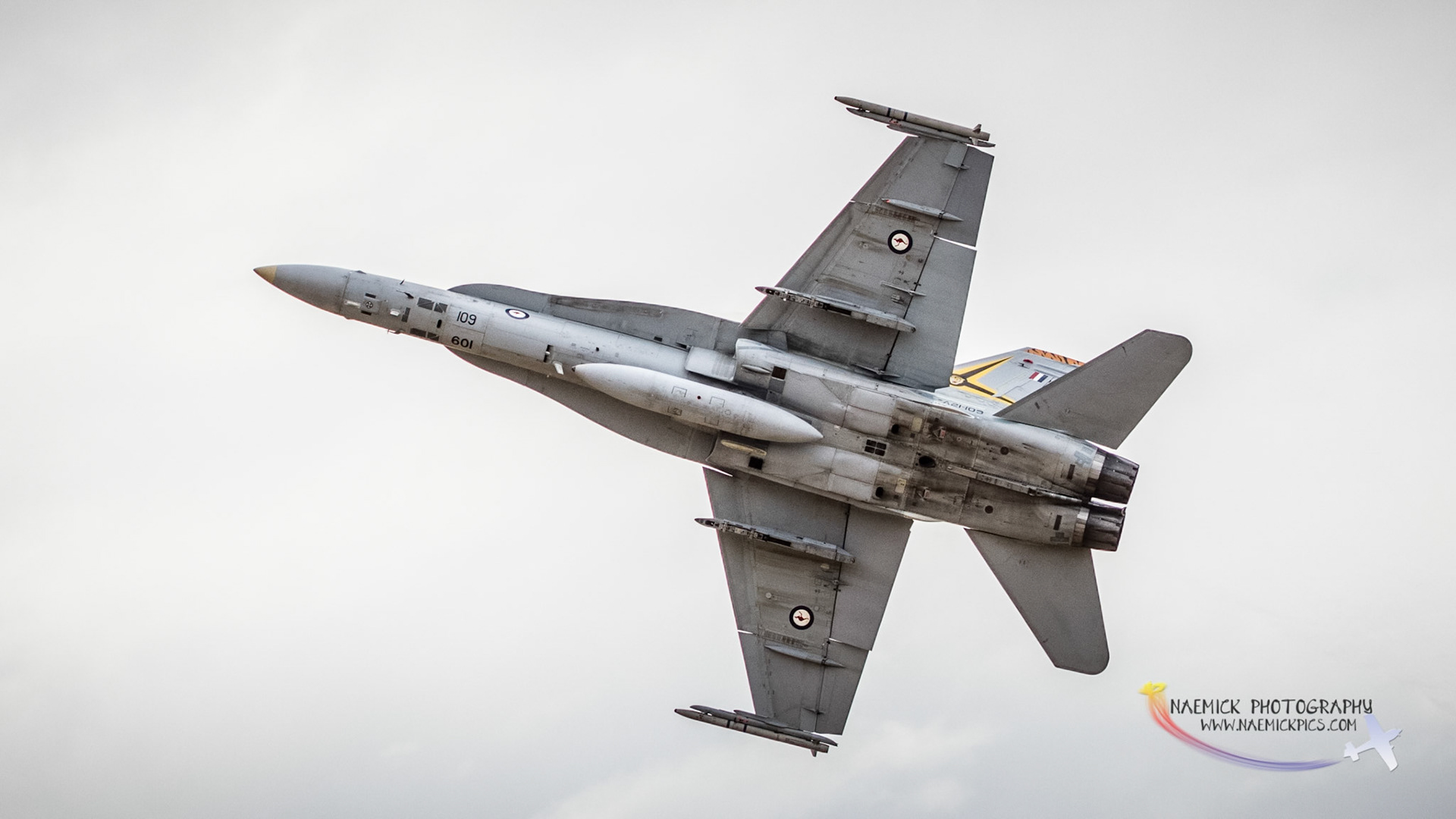 A military jet, likely a McDonnell Douglas F/A-18 Hornet, performs an aerial maneuver against a plain sky background. It features visible numbers "109" and "601".