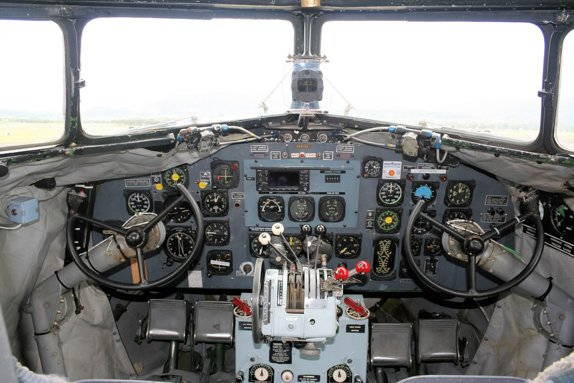 The cockpit of a historic aircraft is visible, showing a complex instrument panel, control yokes, and various levers.
