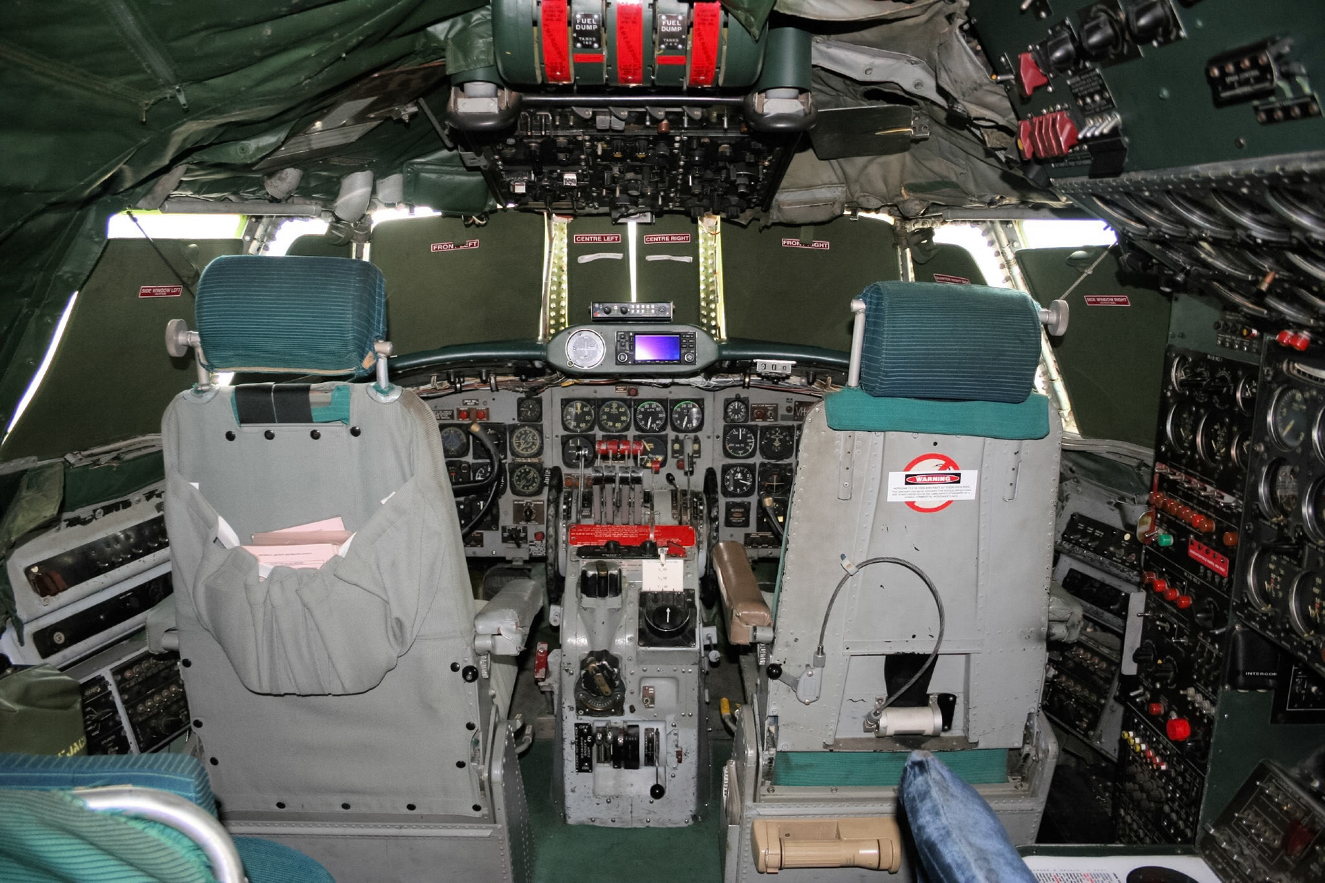 The cockpit of a vintage aircraft with numerous gauges, switches, and two pilot seats. A "WARNING" label is visible.