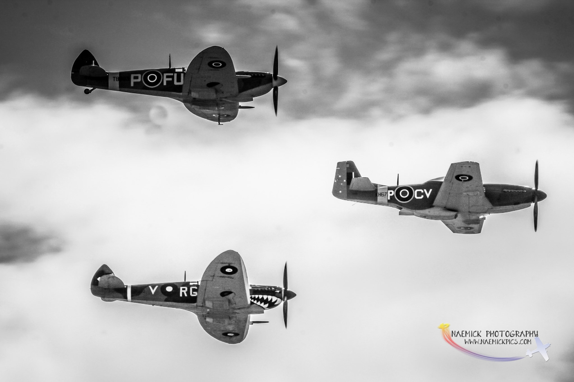 Three historic fighter aircraft, two Supermarine Spitfires and one P-51 Mustang, perform an aerial display against a cloudy sky.