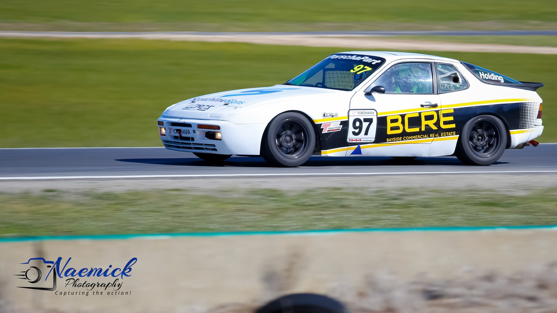 A white Porsche 944 racing car with number 97 and "BCRE" sponsorship drives on a track in Victoria, Australia.
