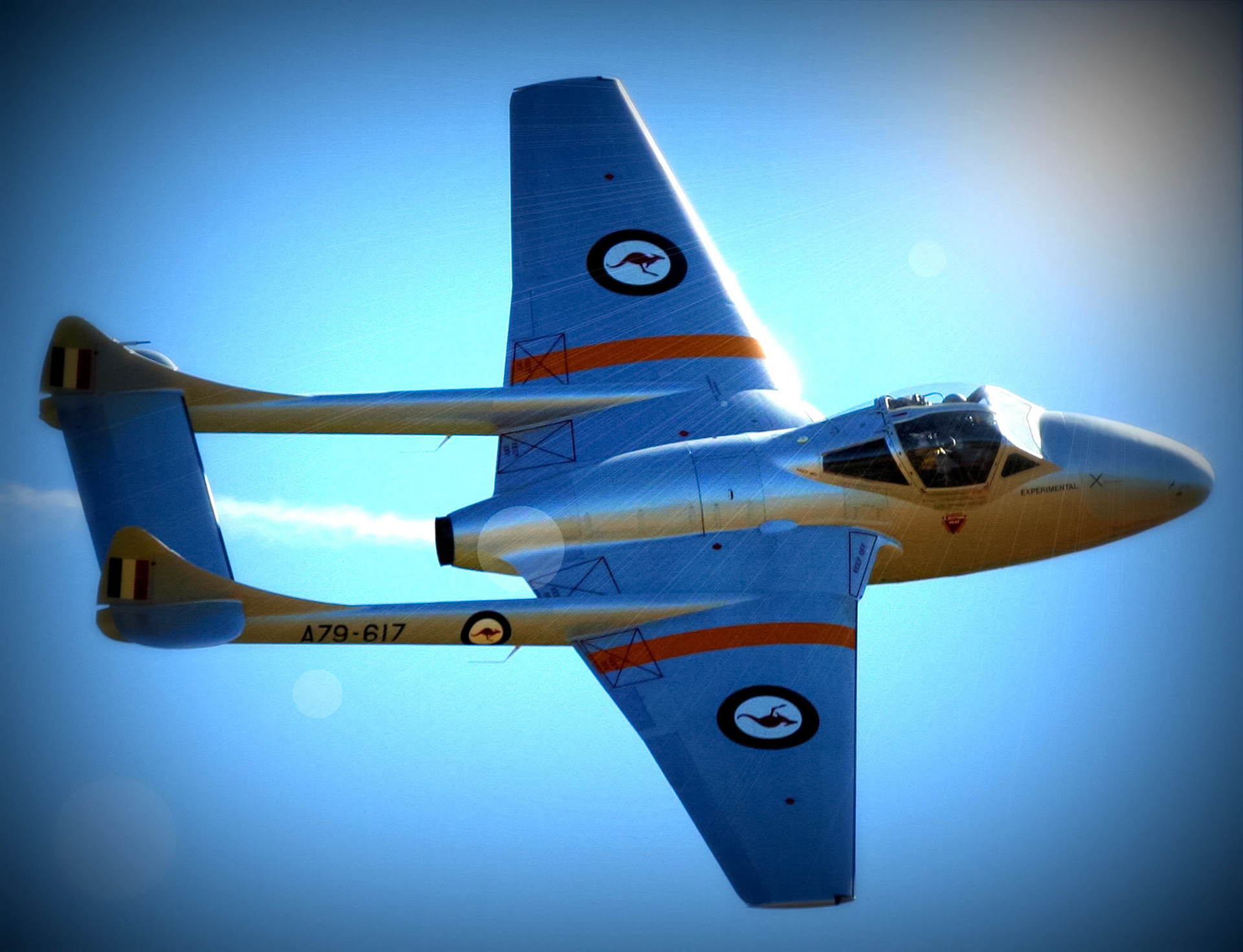 A de Havilland Vampire jet aircraft, marked with "A79-617" and Australian insignias, in flight against a clear blue sky. The aircraft also bears the text "EXPERIMENTAL".