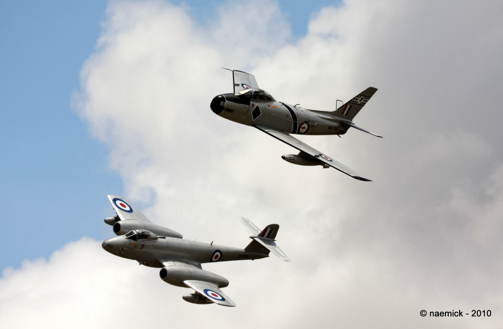 Two historic military jets, a North American F-86 Sabre and a Gloster Meteor, fly against a cloudy sky.