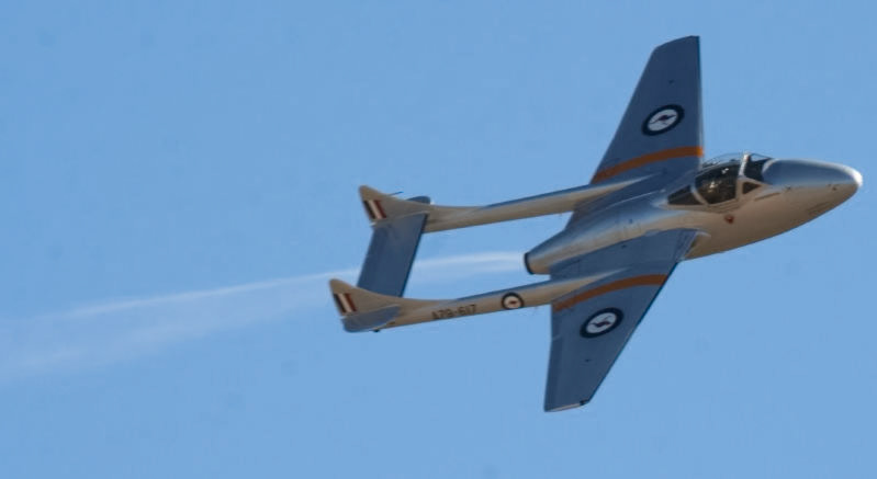 A de Havilland Vampire aircraft, model FB.31, registration "A79-617", flies against a clear blue sky, leaving a contrail.