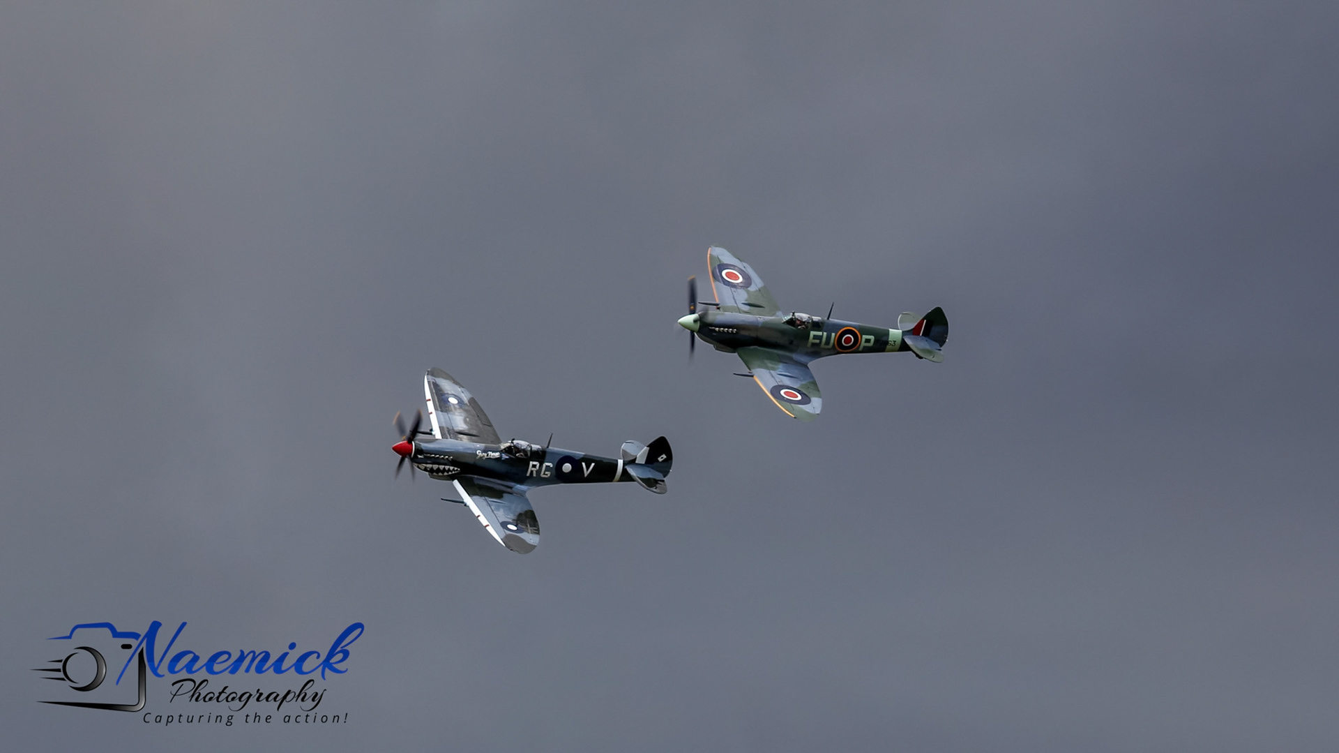 Two Supermarine Spitfire aircraft, one with "FUOP" and the other with "RG V" markings, fly in formation over Temora, New South Wales, Australia.