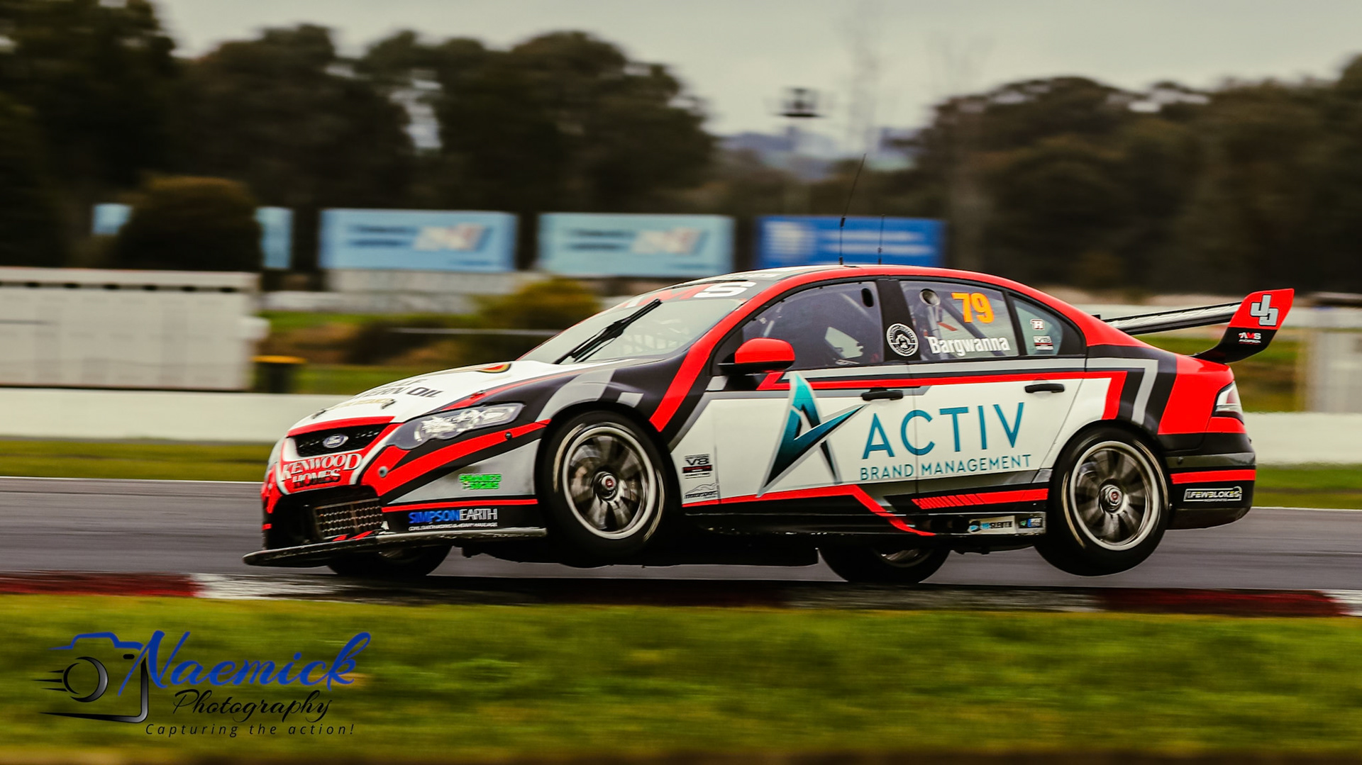 A Ford Falcon V8 Supercar, number "79" driven by Bargwanna, navigates a turn on a racetrack in Victoria, Australia.
