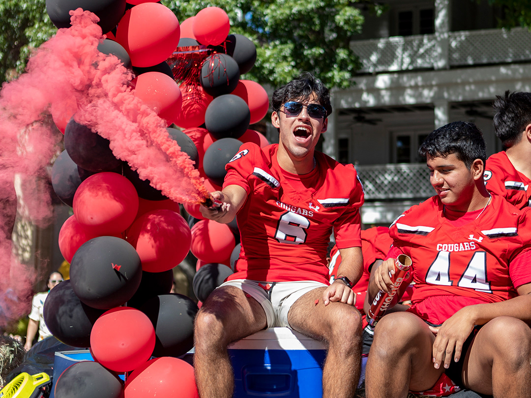 A Canyon HS football player holds a red smoke canister while riding on a float during the Comal County Fair parade at Main Plaza on Sept. 27, 2024. BLAINE YOUNG | Herald-Zeitung
