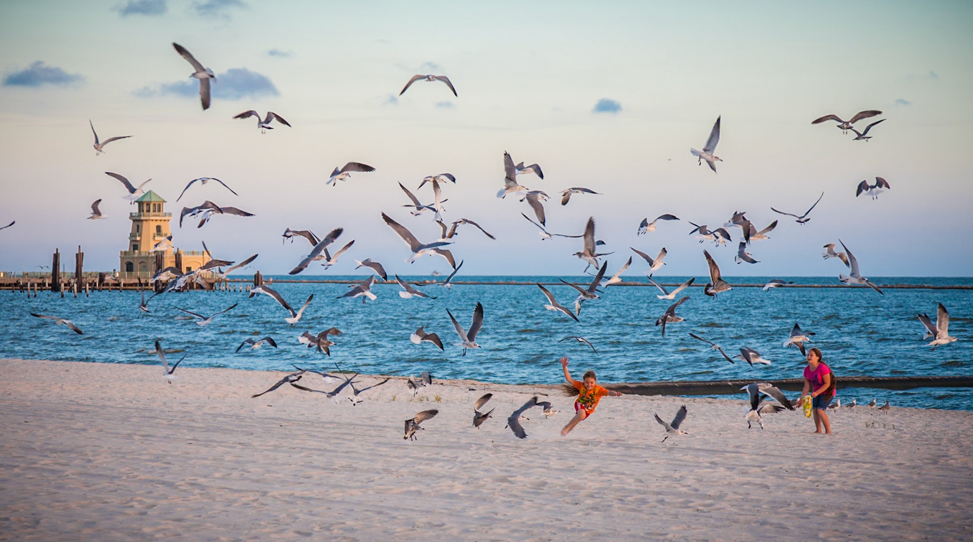 141011_083 Two girls tossing bread crumbs to seagulls on the beach in Biloxi, Mississippi