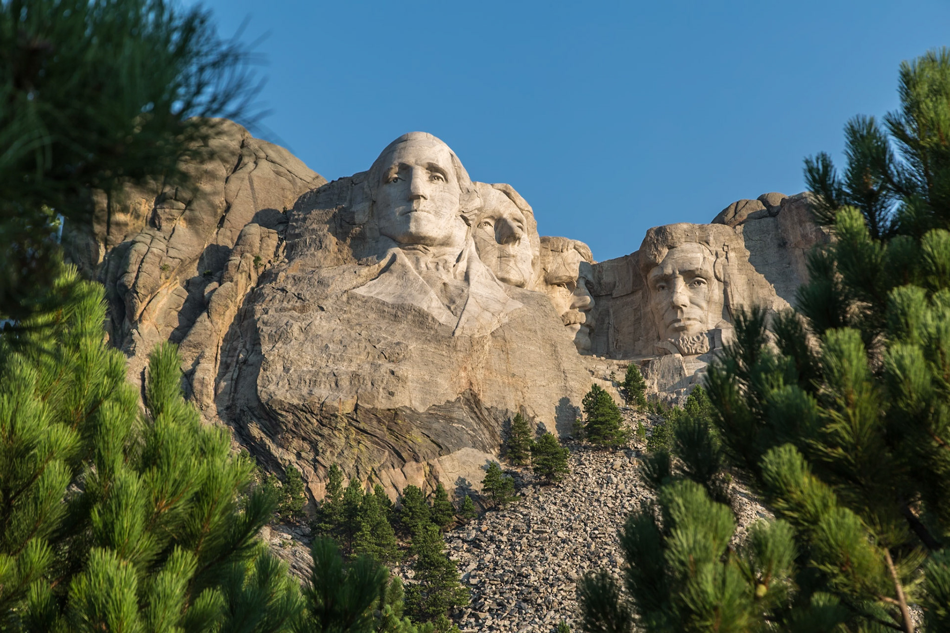 180816_029 Carved granite busts of George Washington, Thomas Jefferson, Theodore "Teddy" Roosevelt and Abraham Lincoln framed by pine trees at Mount Rushmore National Monument near Keystone, South Dakota
