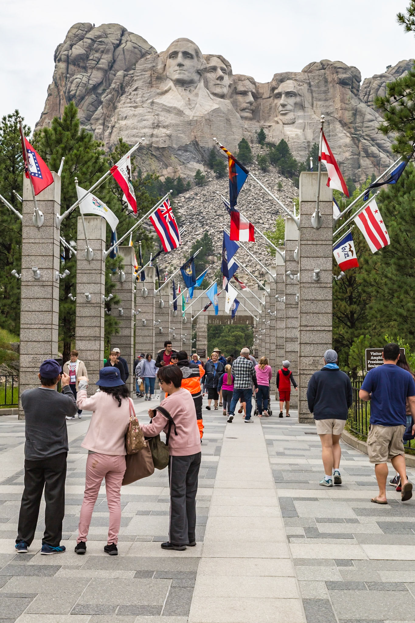 180814_085 Tourists admire the carved granite busts of George Washington, Thomas Jefferson, Theodore "Teddy" Roosevelt and Abraham Lincoln above the Avenue of Flags at the entrance to Mount Rushmore National Monument near Keystone, South Dakota