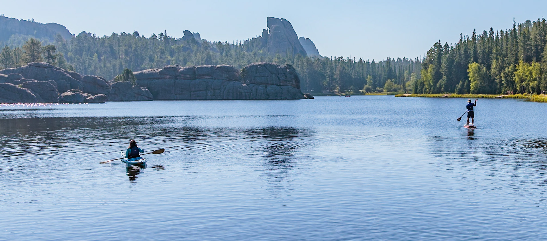 240817_068 Paddleboarder and kayak navigating the calm waters of Sylvan Lake in Custer State Park, South Dakota, USA