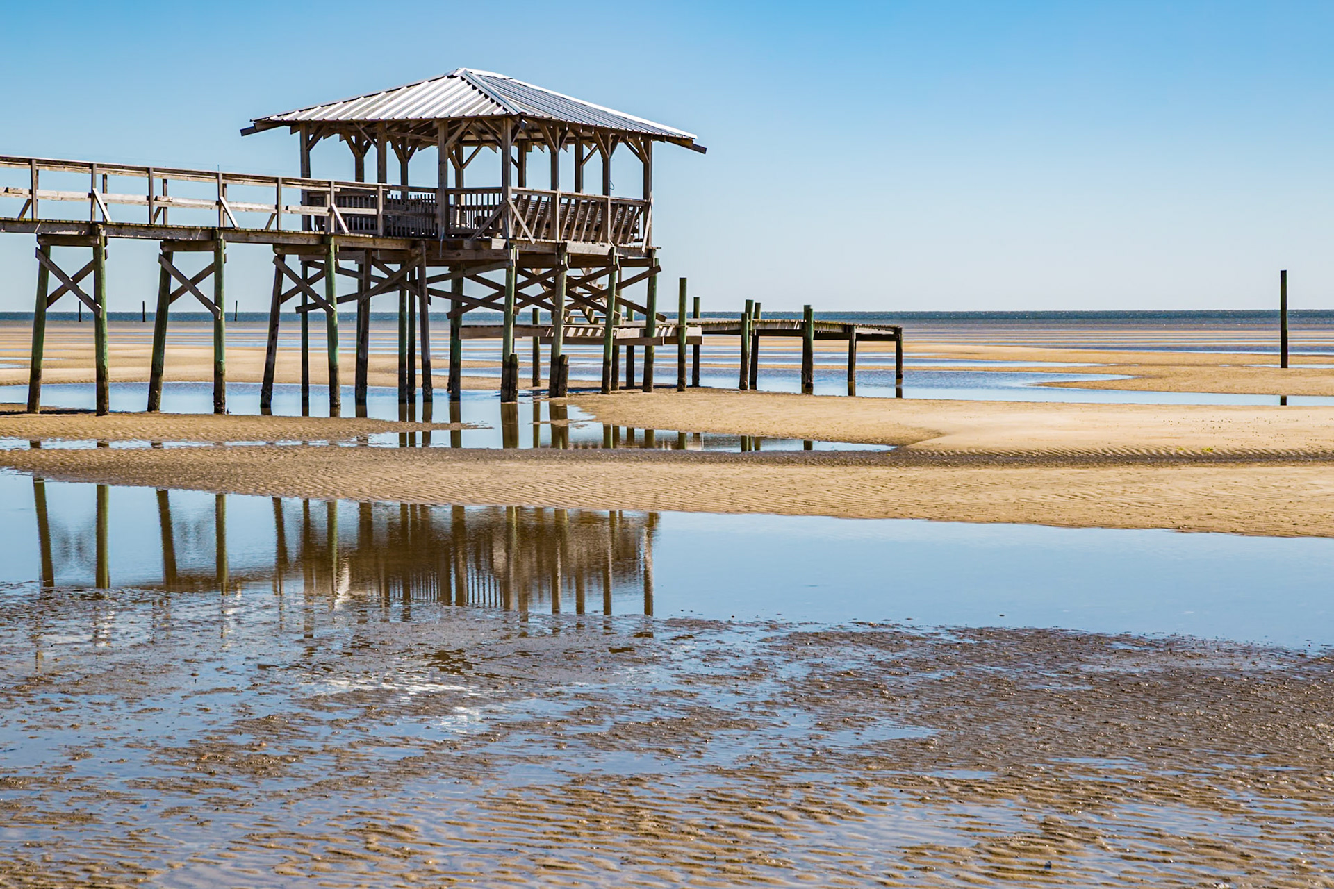 150218_100 Old dilapidated wooden dock, boathouse, and pier stands above tide pools on the Waveland, Mississippi beach at low tide.