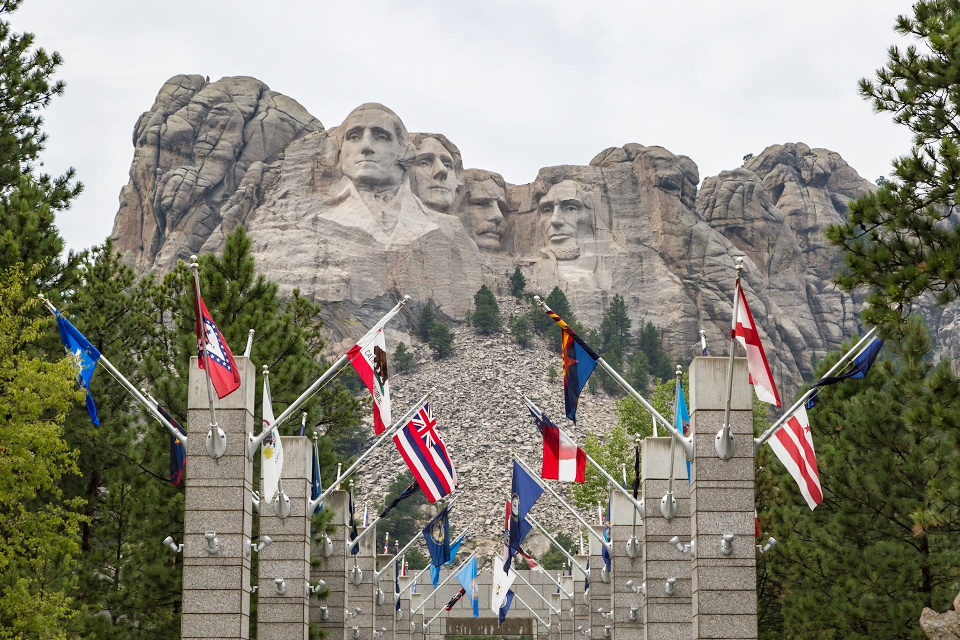 180814_084 Carved granite busts of George Washington, Thomas Jefferson, Theodore "Teddy" Roosevelt and Abraham Lincoln above the Avenue of Flags at the entrance to Mount Rushmore National Monument near Keystone, South Dakota