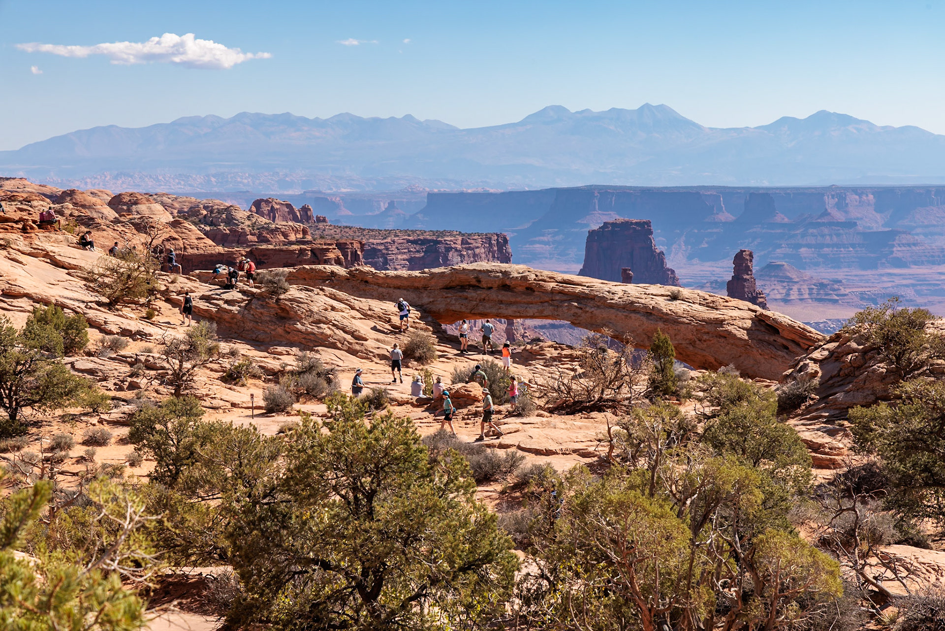 240928_029 Tourists walking on the rock formations at Mesa Arch in the  Island in the Sky area of Canyonlands National Park, Utah, USA