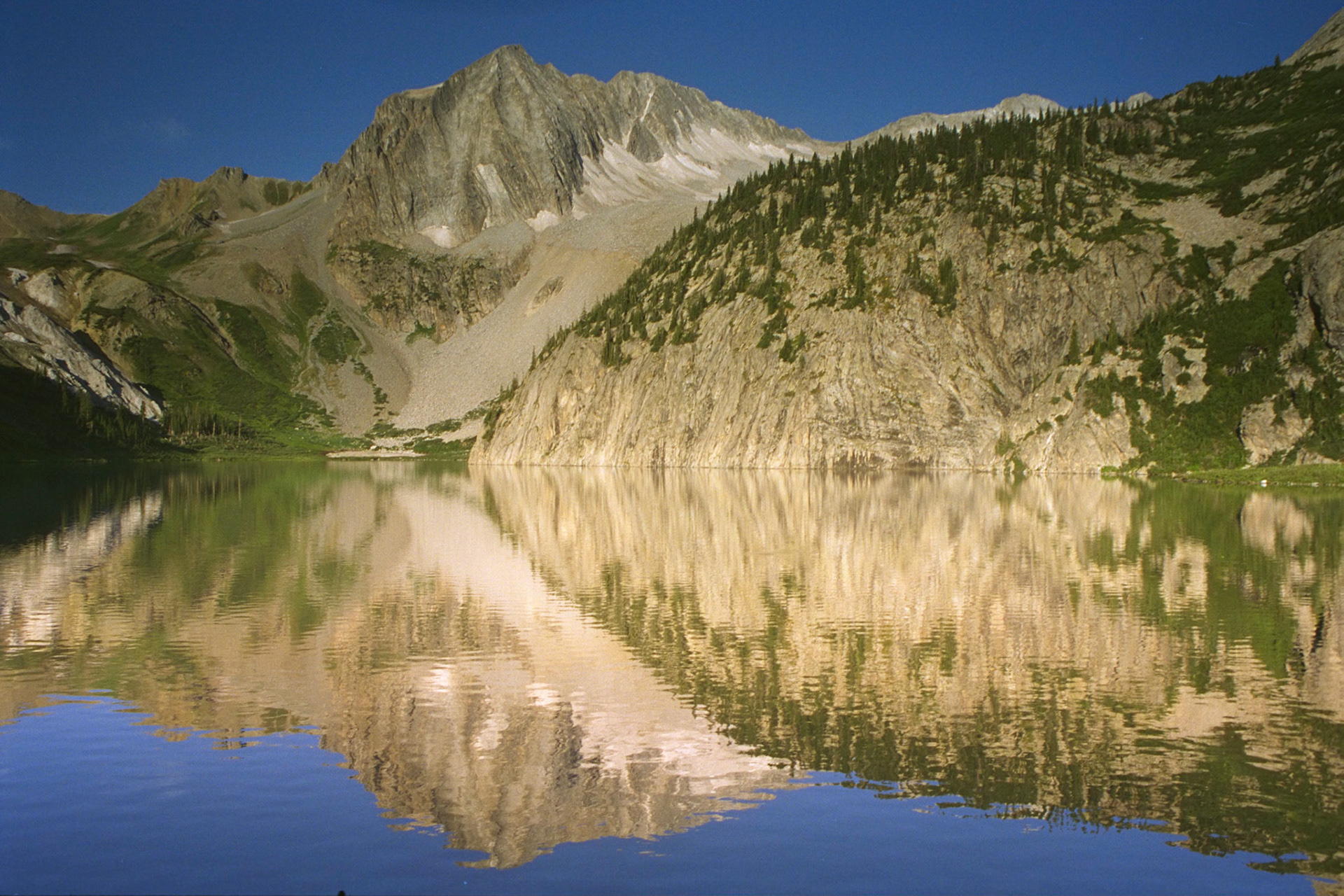 A view of Snowmass Mountain reflected in Snowmass Lake in the mid-morning. Snowmass Mountain is a 14,000 ft. peak in the Maroon Bells Wilderness in Colorado. This view was especially welcome as I and my backpacking partner had to hump over three or four 12,000 ft passes in as many days. We camped along this lake for two nights.