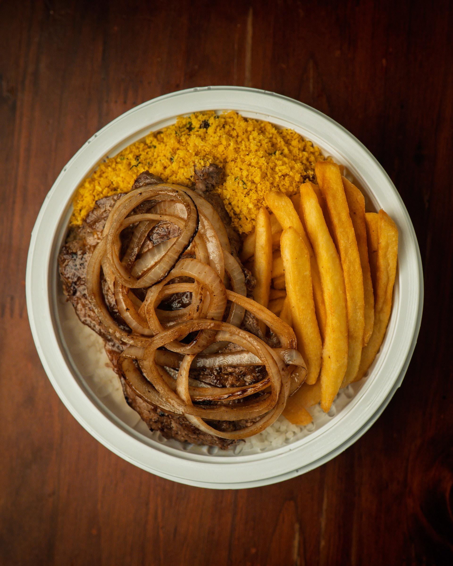 Marmita de bife acebolado com farofa e batata frita, servida em ângulo que mostra o volume da embalagem.