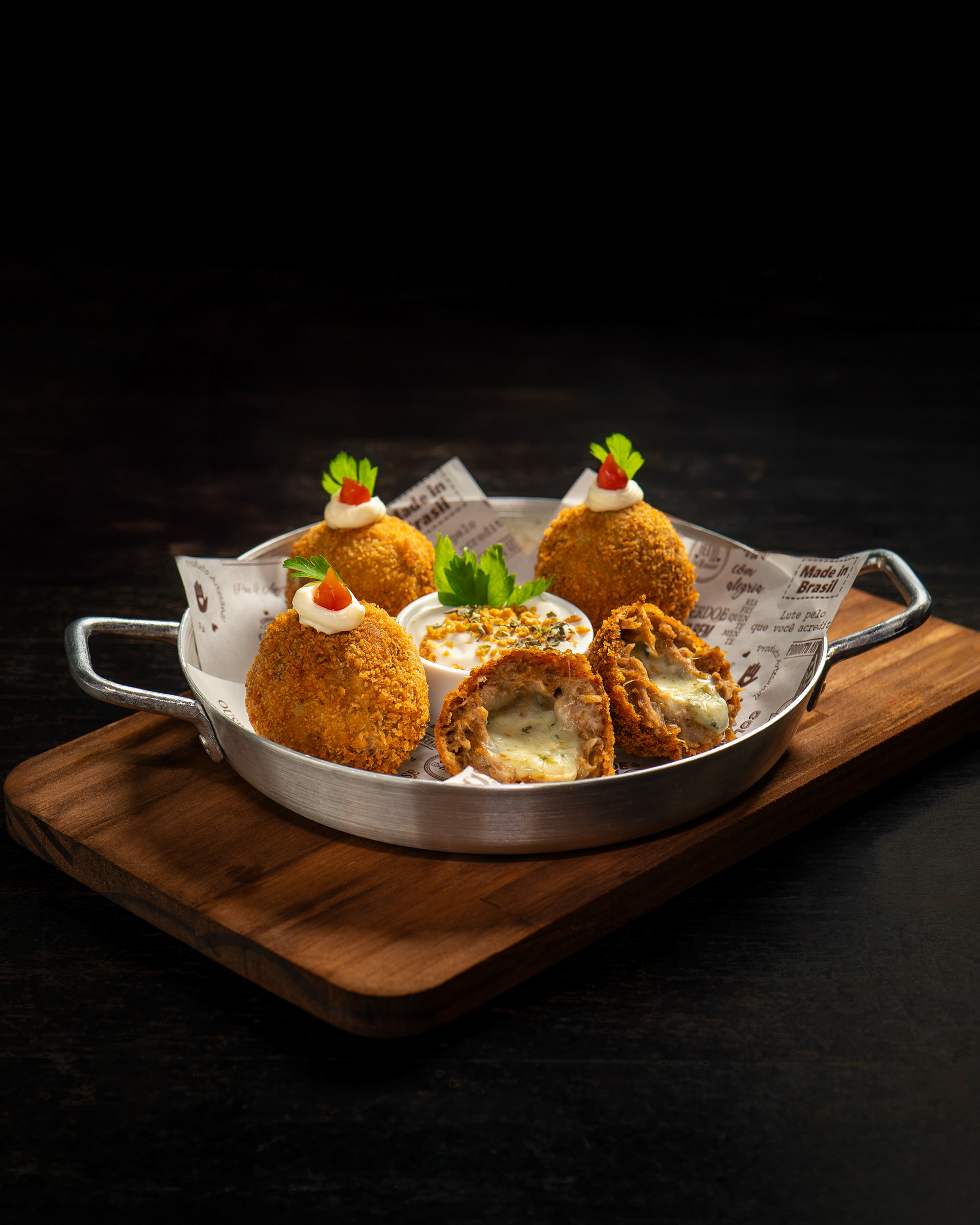 Bolinhos de costela recheados com queijo cremoso, um deles cortado, servidos em travessa metálica com molho de acompanhamento.