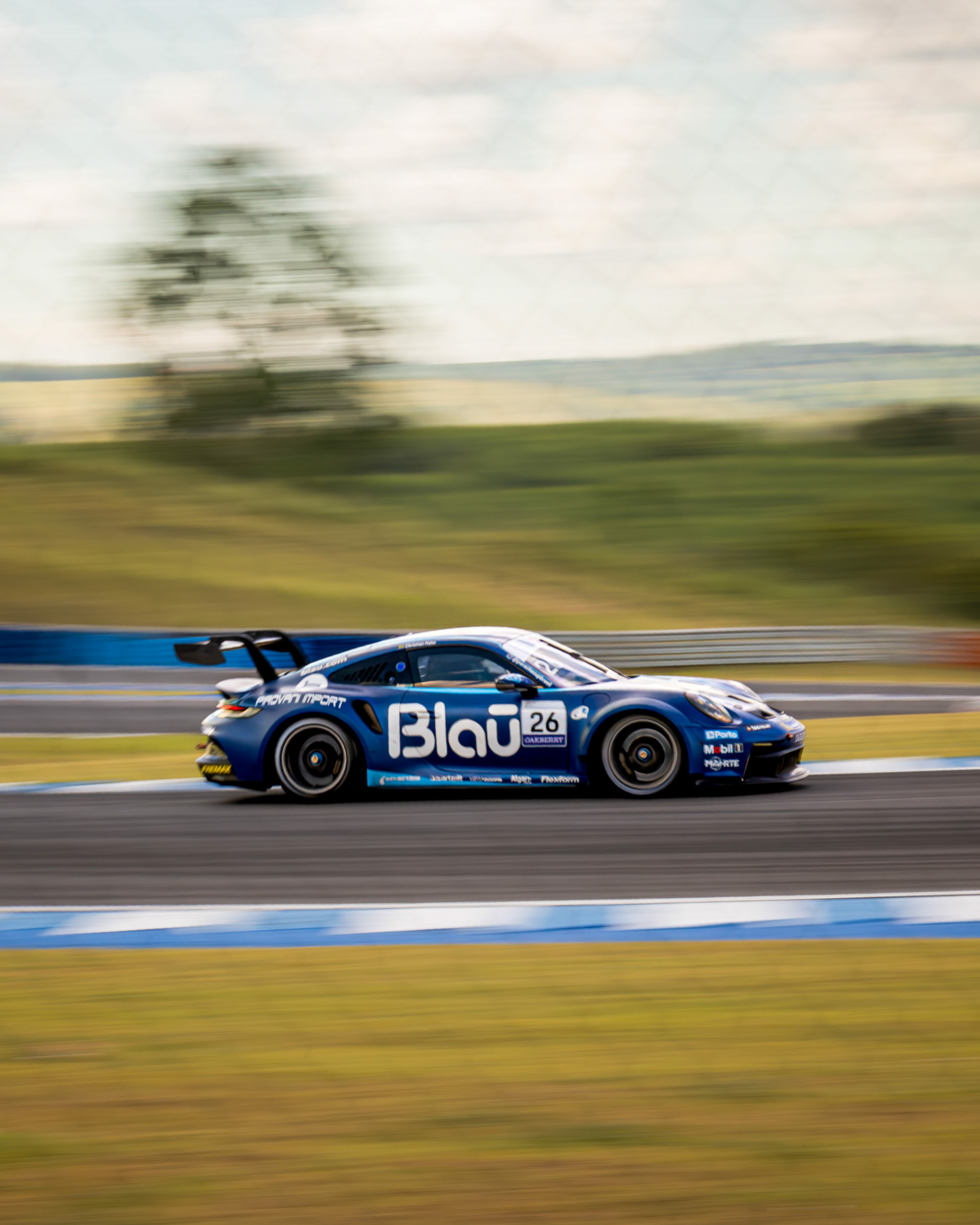 Carro de corrida Porsche 911 GT3 Cup azul (nº 26) em alta velocidade na pista do Autódromo Velocitta, capturado com técnica de panning.