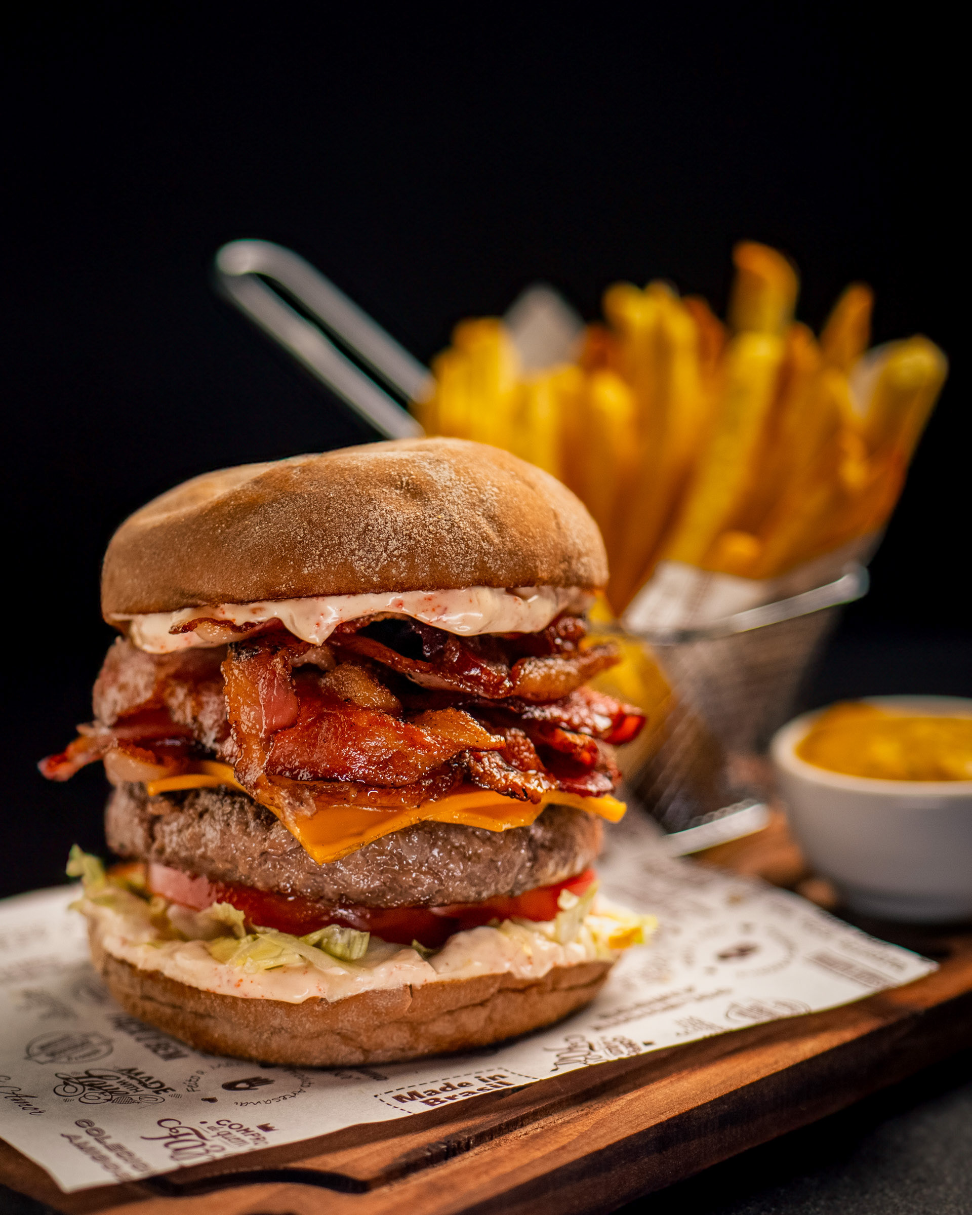 Hambúrguer X-Bacon com duplo bife, queijo cheddar derretido e batatas fritas em uma tábua de madeira
