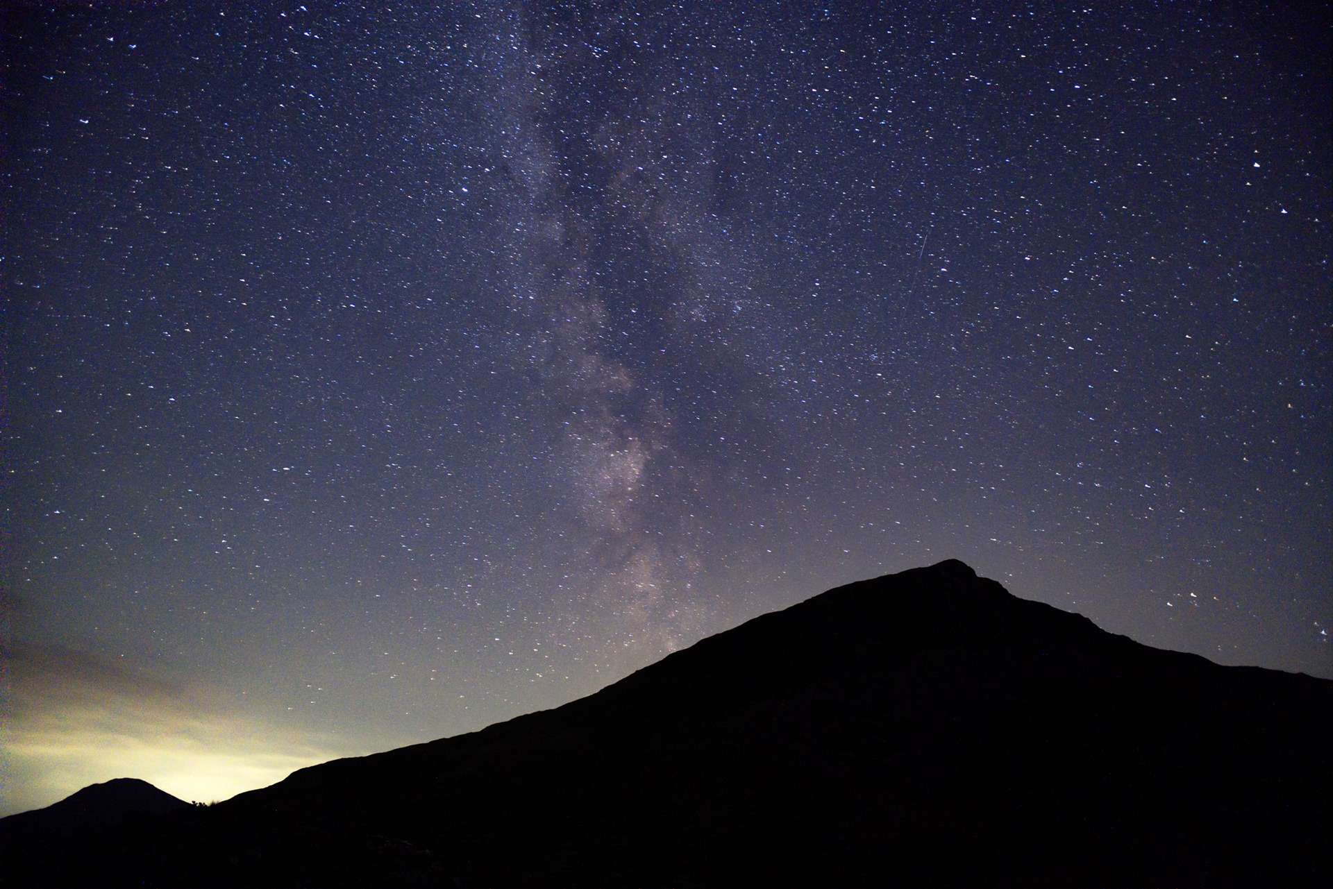 The Milky Way rising above a dark mountain silhouette and a softly glowing horizon.