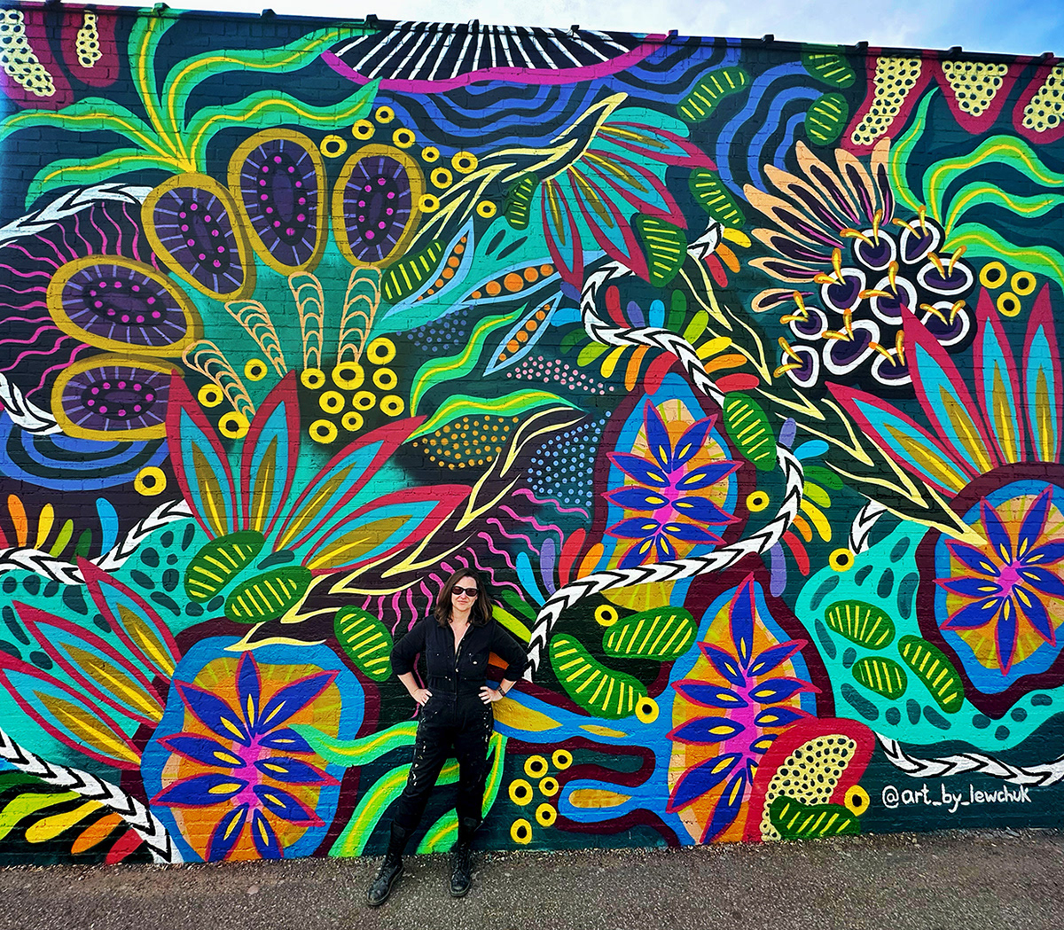 me wearing all black standing in front of large detailed abstract botanical tropical mural