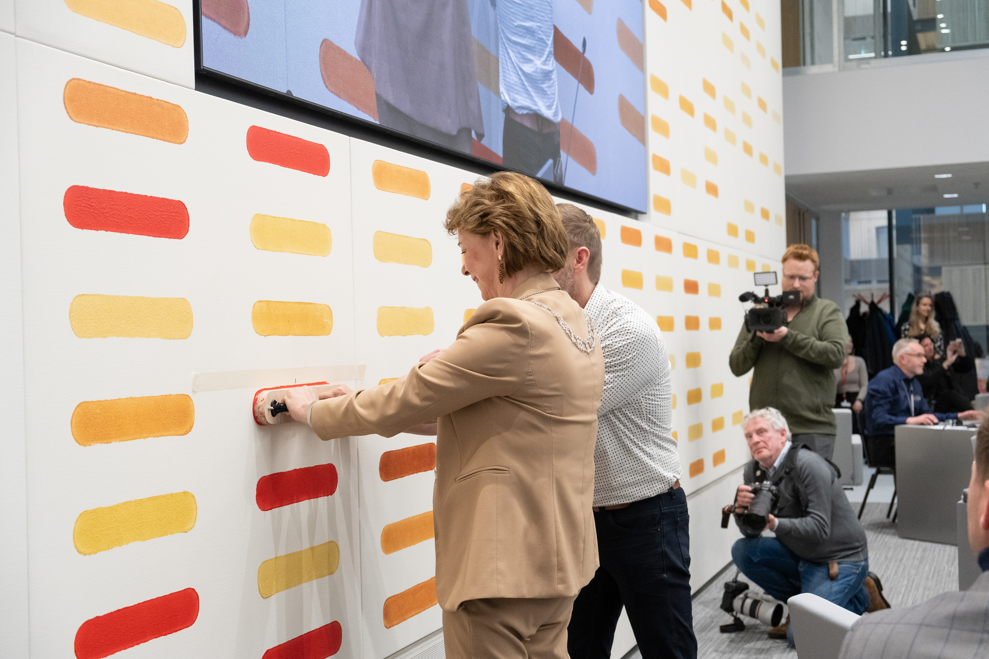 Onder begeleiding van de Nederlandse kunstenaar Maurice van Venrooij plaatst burgemeester Elly Blanksma de laatste stempel op de muurschildering, ontwerp Maurice van Venrooij, in de raadzaal van het Huis voor de Stad in Helmond.