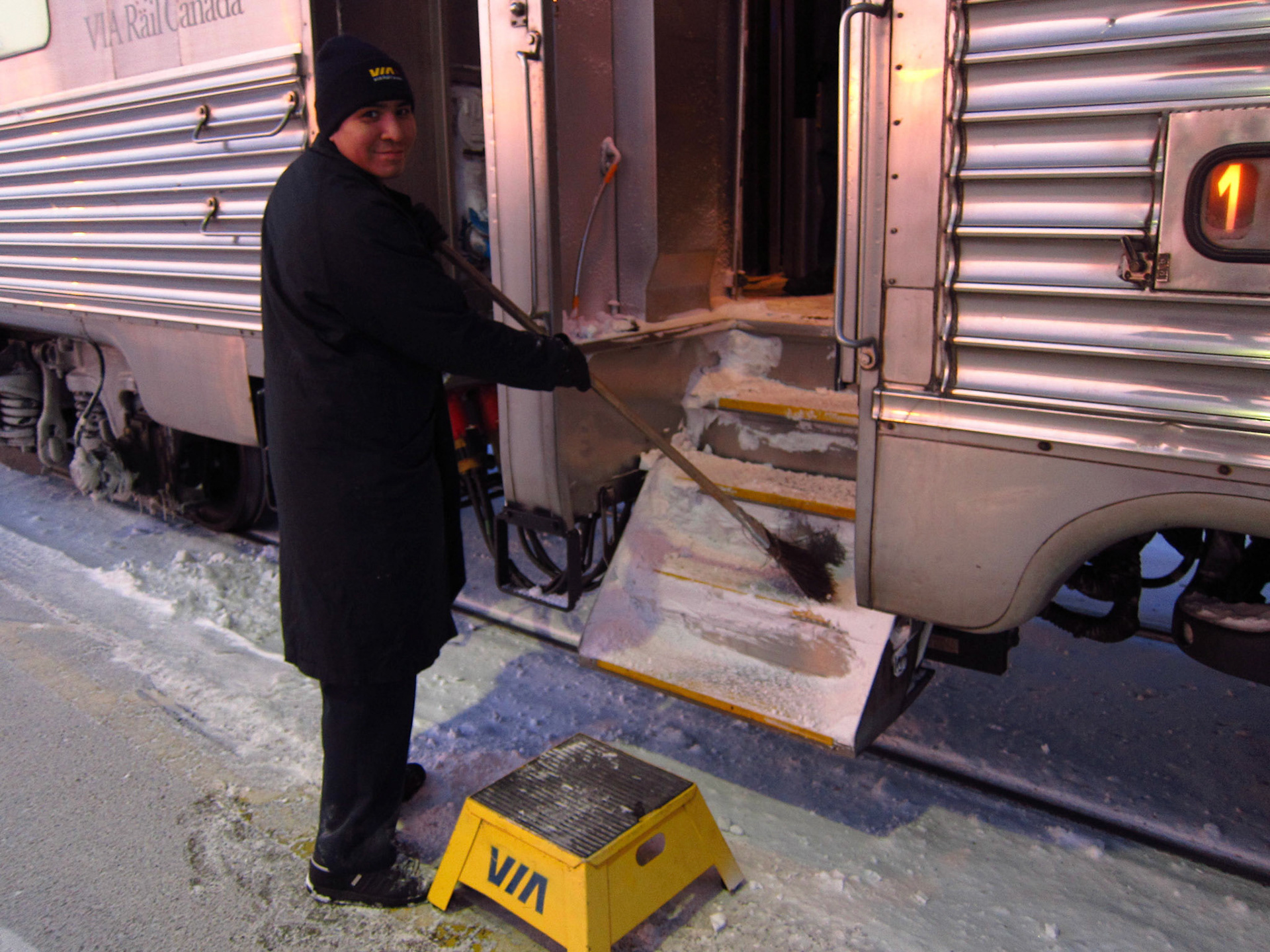 Pierre, a VIA crew member, clears the snow that has piled up in the doorway