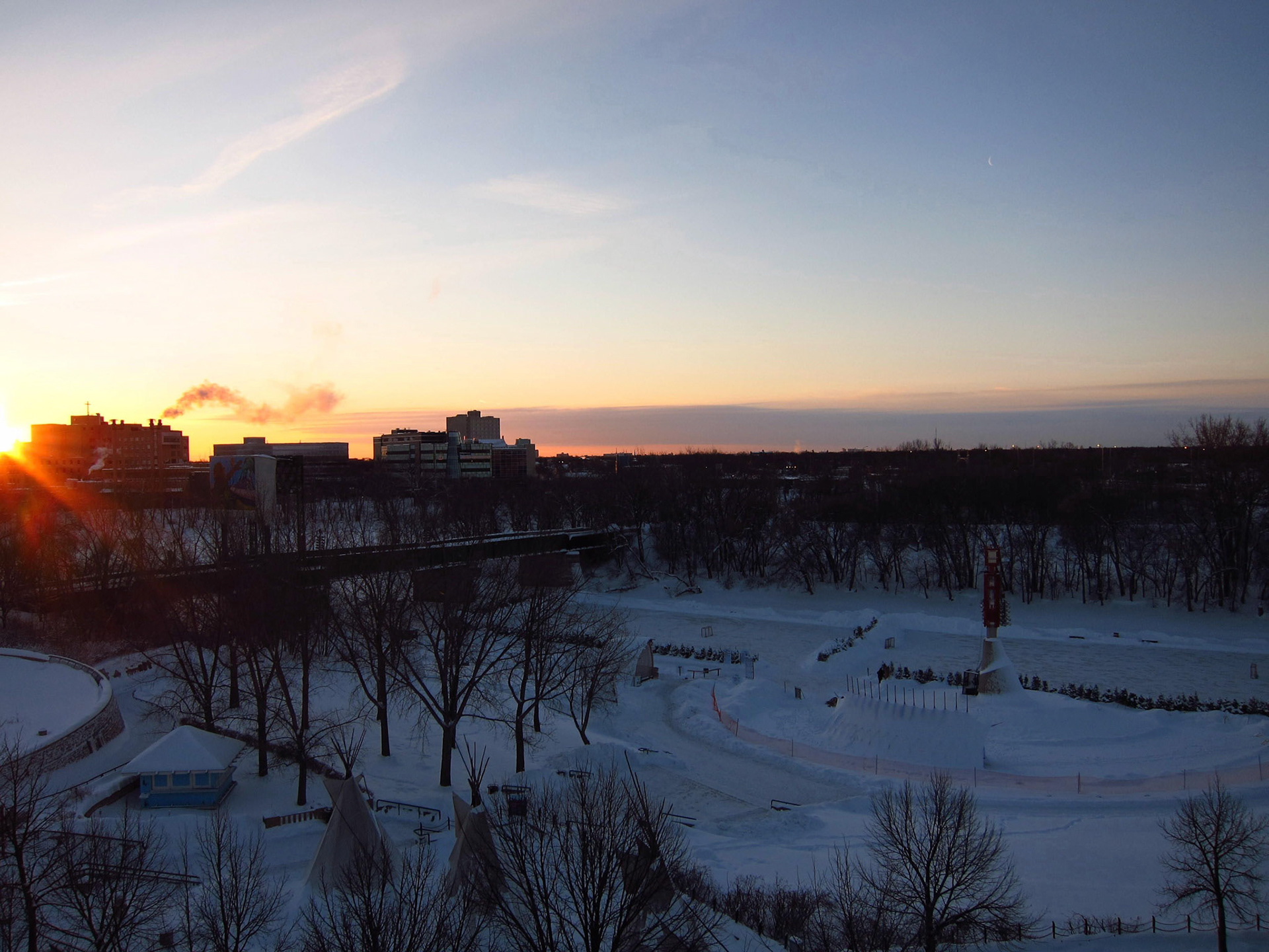 The sun rises over the Forks of the Red and Assiniboine Rivers. You can see hockey rinks groomed on the river!