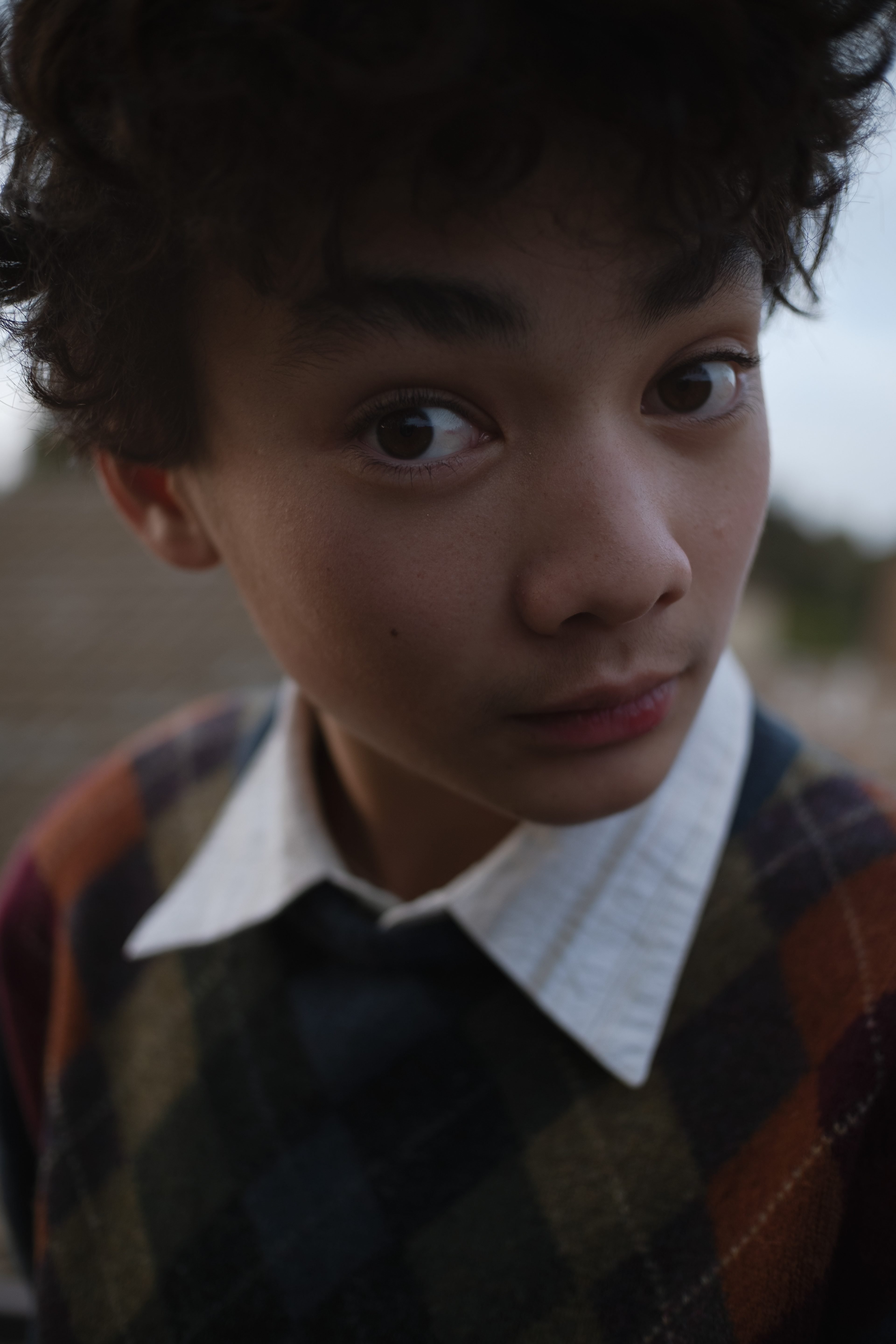 Outdoor portrait of curly hair teen boy with white collared shirt and argyle sweater.