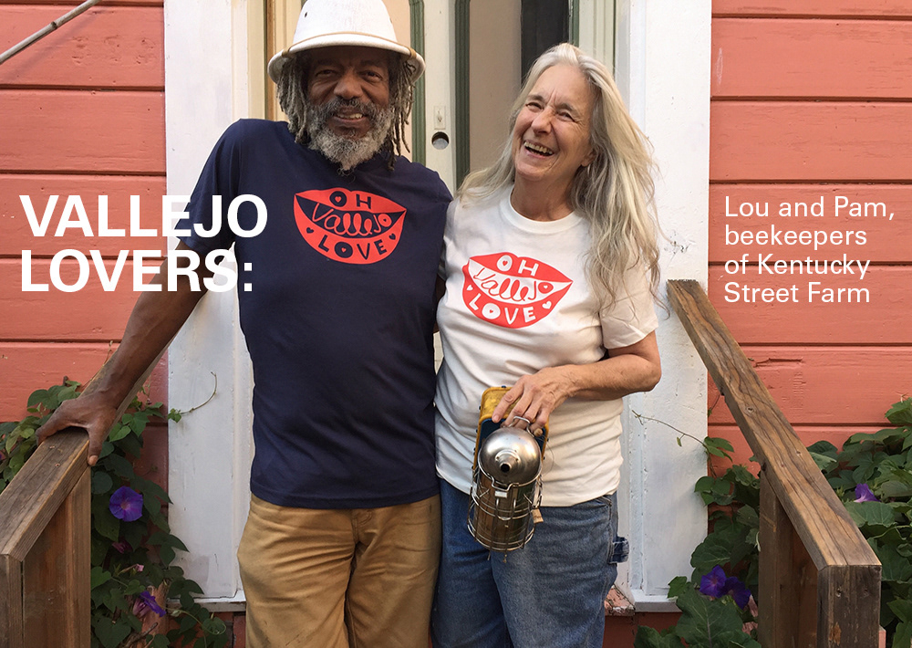 Lou and Pam, beekeepers of Kentucky Street Farm in Vallejo wearing two different colors of Oh Vallejo Love tees and smiling. Pam holds a smoker.