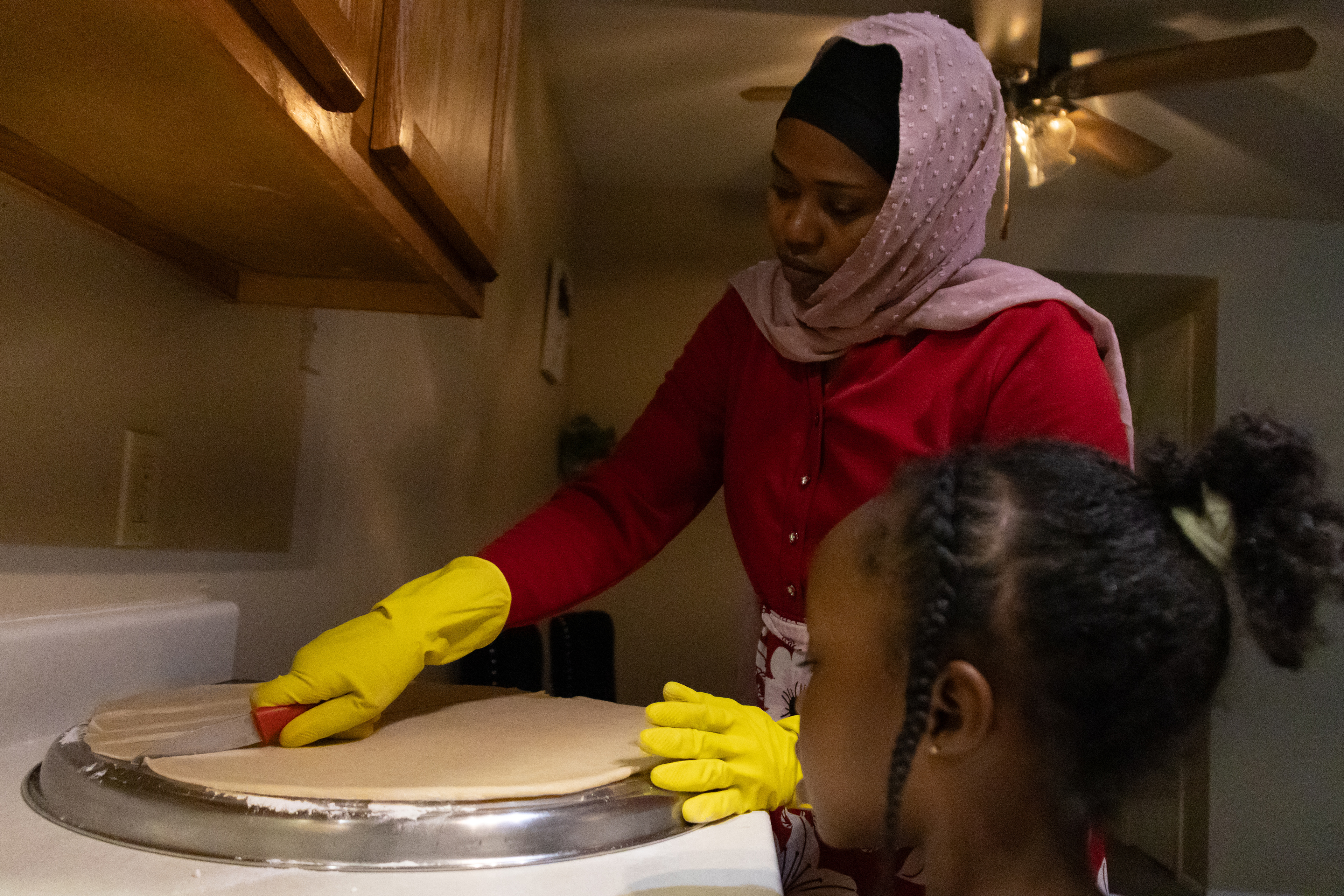 Aisha Ibrahim cuts Sudanese fatira into strips in her kitchen as her daughter, Buraga Abdul, 6, watches on Saturday, Feb. 23, 2025, in Lincoln, Neb. Sudanese Fatira is a bread-like food eaten with tea or coffee. Ibrahim made the dough from scratch, rolled it out, then cut it into strips.
