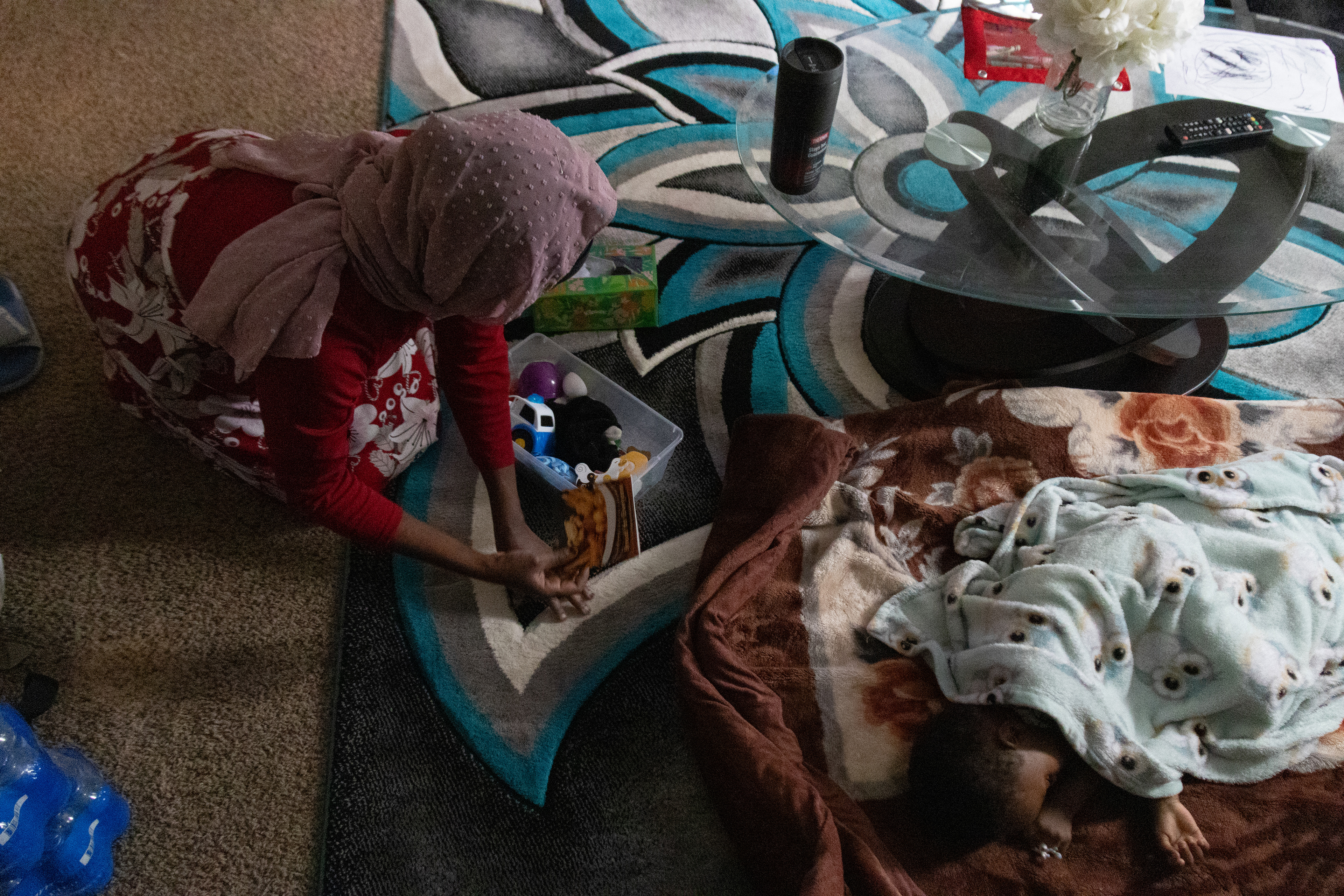 Aisha Ibrahim, 30, gathers toys from the living room carpet as her son, Bugala Abdul, sleeps nearby on Saturday, Feb. 23, 2025, in Lincoln, Neb. Ibrahim must clean quickly while her two children sleep since she has guests visiting in the evening.