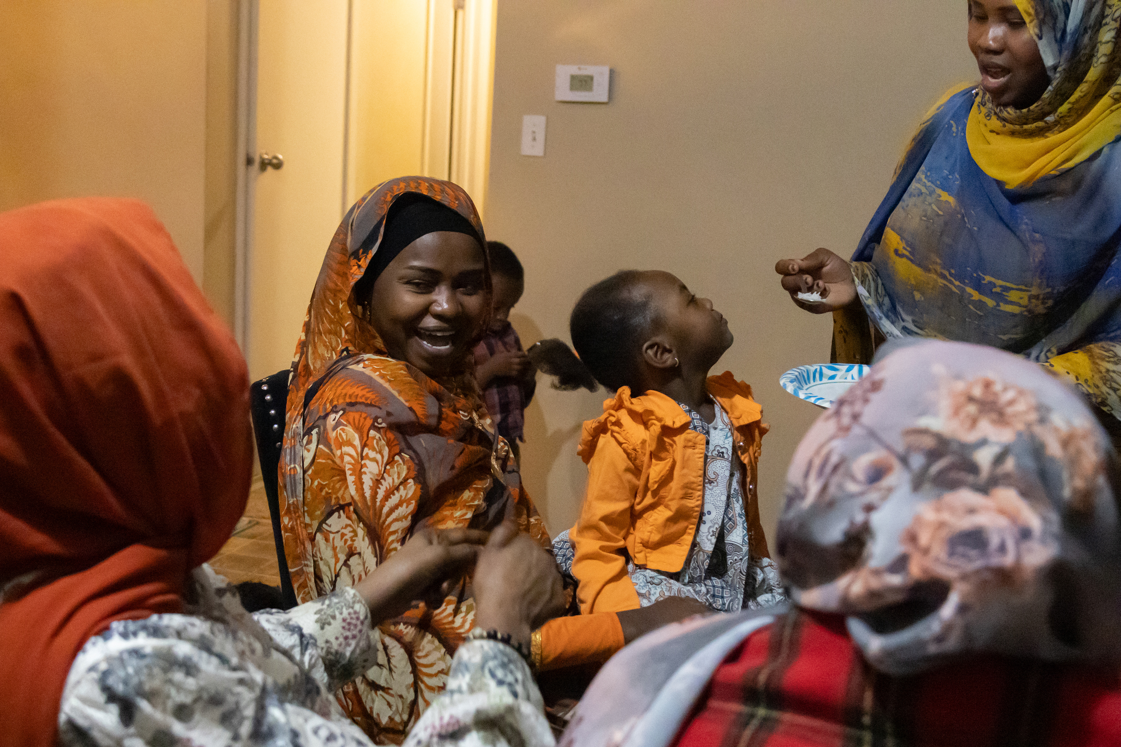 Aisha Ibrahim, holds her friend’s daughter, Rania Haroun, 3, in her lap as Rania’s mother, Hawa Ishag, feeds her daughter on Saturday, Feb. 23, 2025, in Lincoln, Neb. The guests visiting are 12 of the 14 women who make up the “sister get-together,” a group of Sudanese refugee women who meet every two weeks at a different woman’s house to share a meal together.