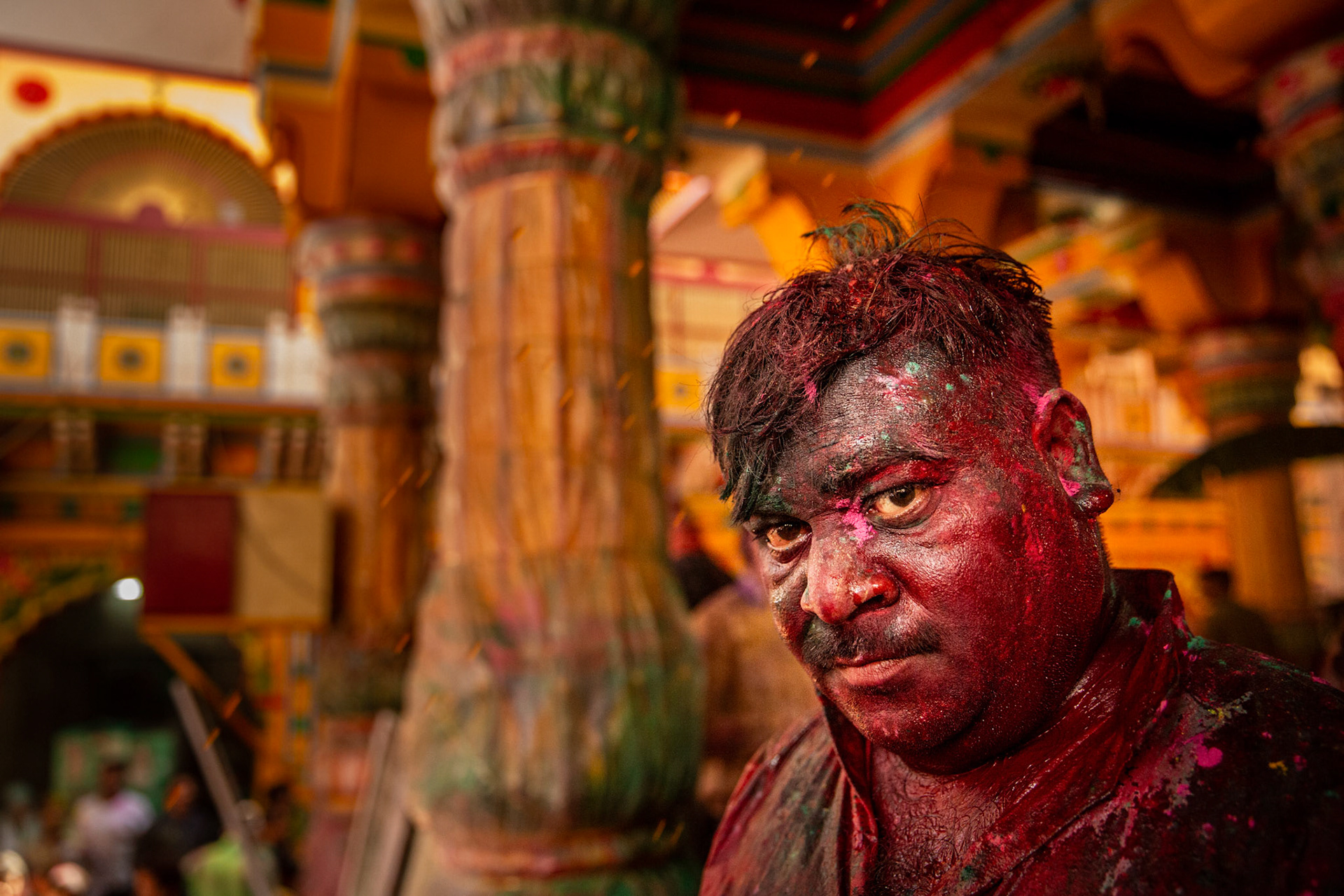 Man covered with gulal and colored water inside Dwarkadhish temple while attending Holi celebrations . Mathura, India