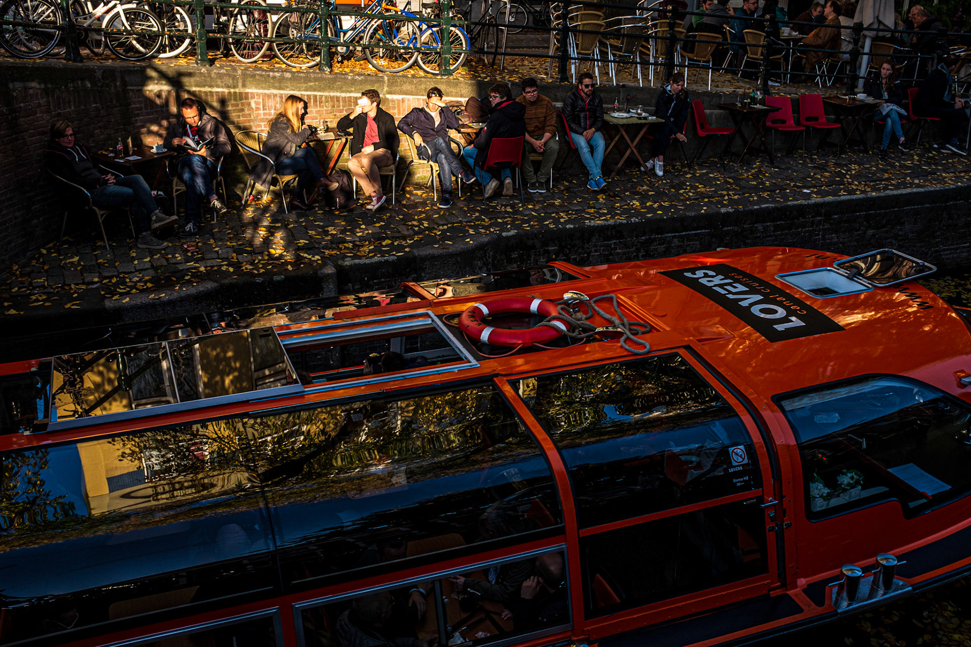 Amsterdam, Netherlands - 31 October 2016: Boat passing in an Amsterdam canal while people chill out on the sidewalk