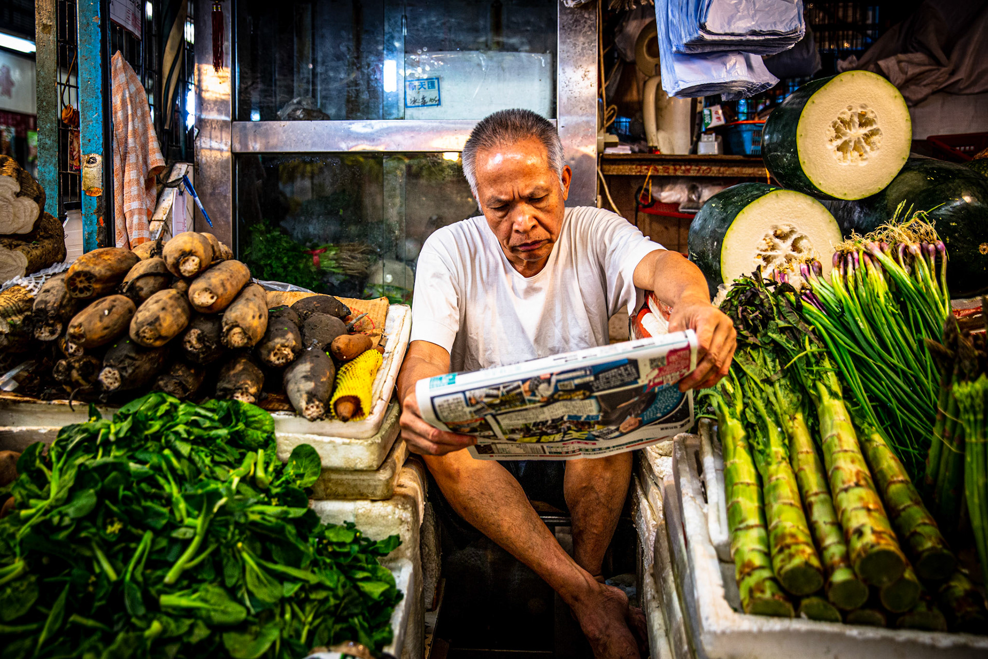 Seller reading the newspaper between his vegetables at Fa Yuen market. Hong Kong