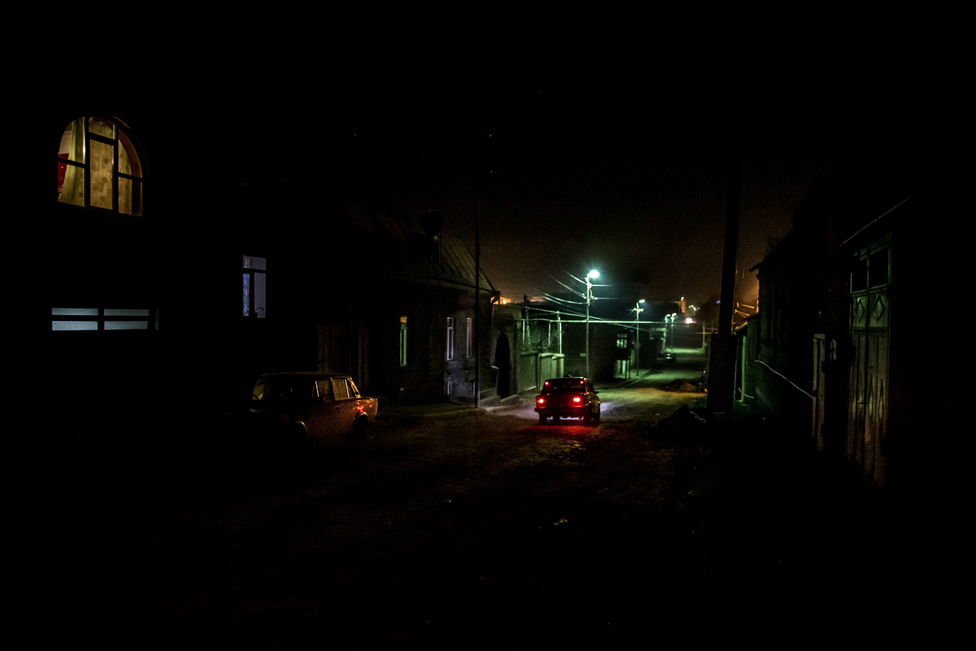 Soviet era car driving past a dark street of Gyumri by night. Armenia
