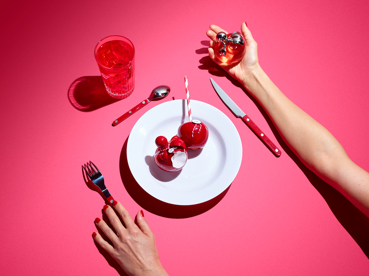 Nina Ricci Parfums : Nina Rouge, nature morte de flacons Nina Ricci dans une assiette avec des couverts et un verre de grenadine rouge sur un fond rose- PALAST PHOTOGRAPHIE, Paris France