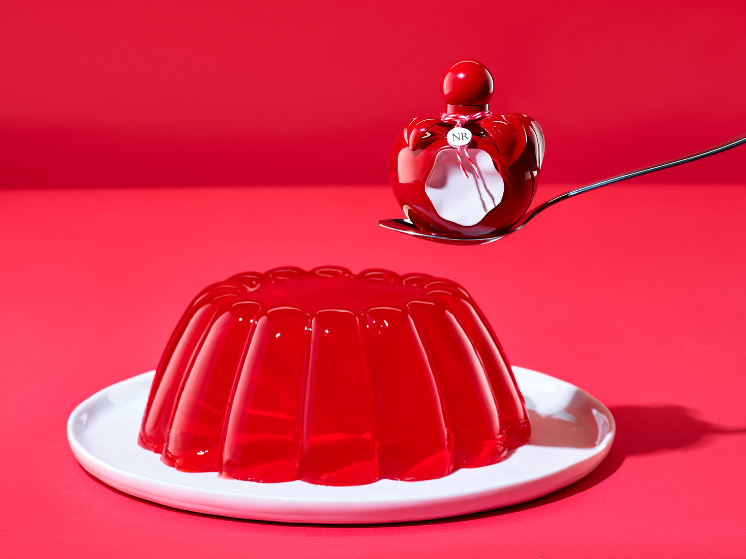 Nina Ricci Parfums : Nina Rouge nature morte parfum Nina Rouge avec gateau de gelée sur fond rouge, color block - PALAST PHOTOGRAPHIE, Paris France