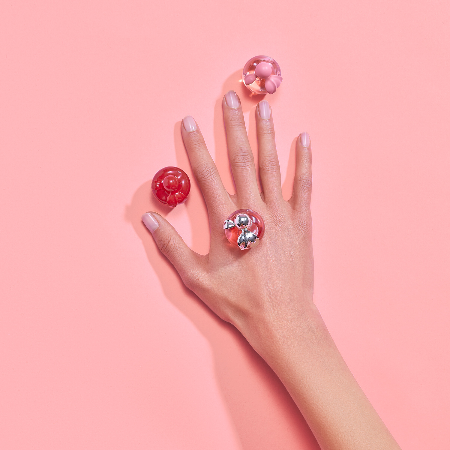 Nina Ricci Parfums : Nina Rouge, photographie de nature morte, parfum, photographie de détail d'une main avec des flacons de parfums miniatures sur un fond rose - PALAST PHOTOGRAPHIE, Paris France