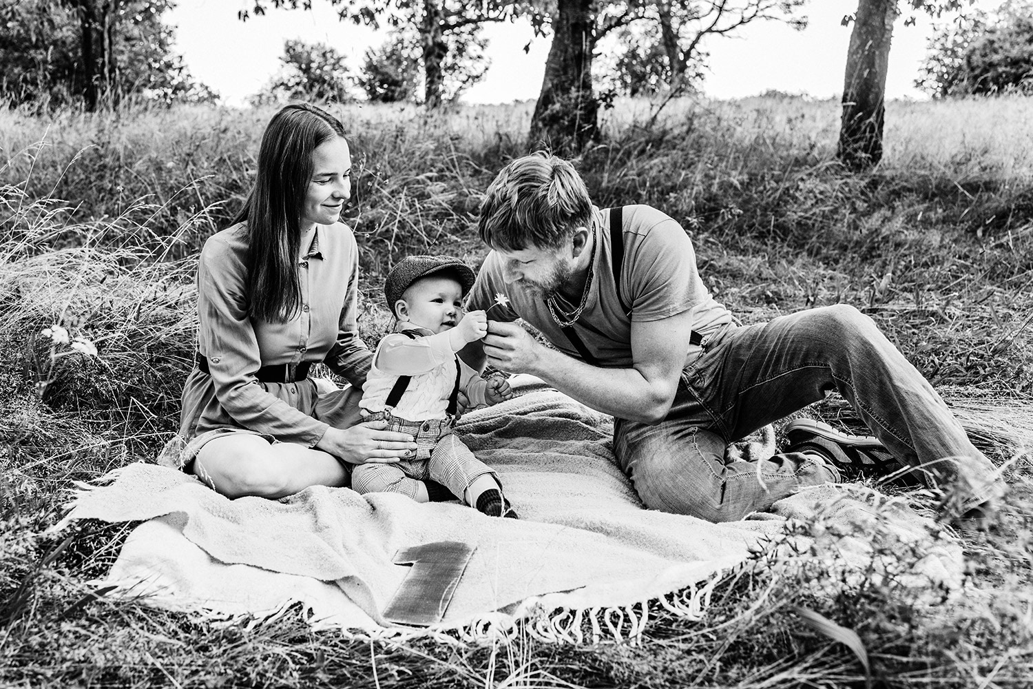 rodiče s chlapečkem si hrají na dece v sadu při letním focení