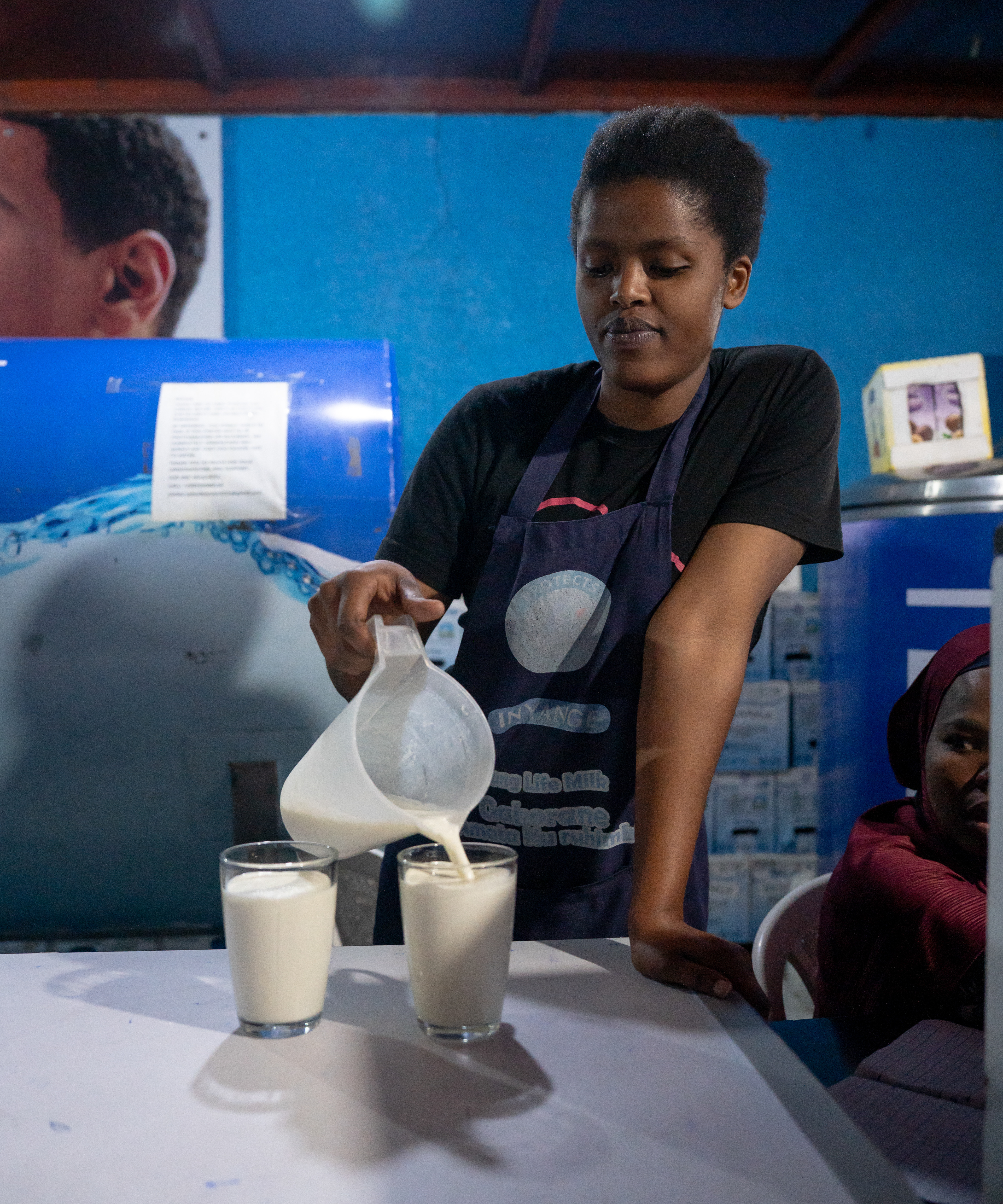 Erinesitine pours milk inside the Inyange Milk Bar on Sunday, May 17, 2026 in Kigali, Rwanda.   Cows have been intrinsic to Rwandan society for centuries as symbols of wealth and status. But during the genocide, cattle herders and cows were killed as Tutsis were historically associated with herding.   President Paul Kagame introduced a program called “Girinka” in 2006 to gift cows to poor families and help the cattle economy rebound following the genocide. Milk production increased and milk bars were started to connect cattle farmers to an increasing urban population, according to the New York Times.   Milk can be served in a variety of ways, including different temperatures and processing types. Inyange is one of Rwanda’s leading dairy and beverage manufacturers. (Photo/Evan Frilingos 2026)