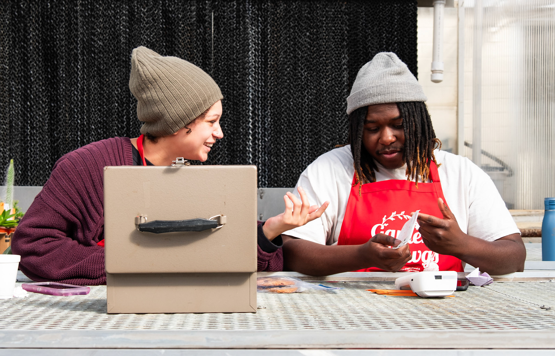 Kailah Keith laughs with Imir Robinson while the two volunteers await customers at the UGA Trial Garden plant sale on Tuesday, Feb. 13, 2024. (Photo/Evan Frilingos; @frilingos.photos)