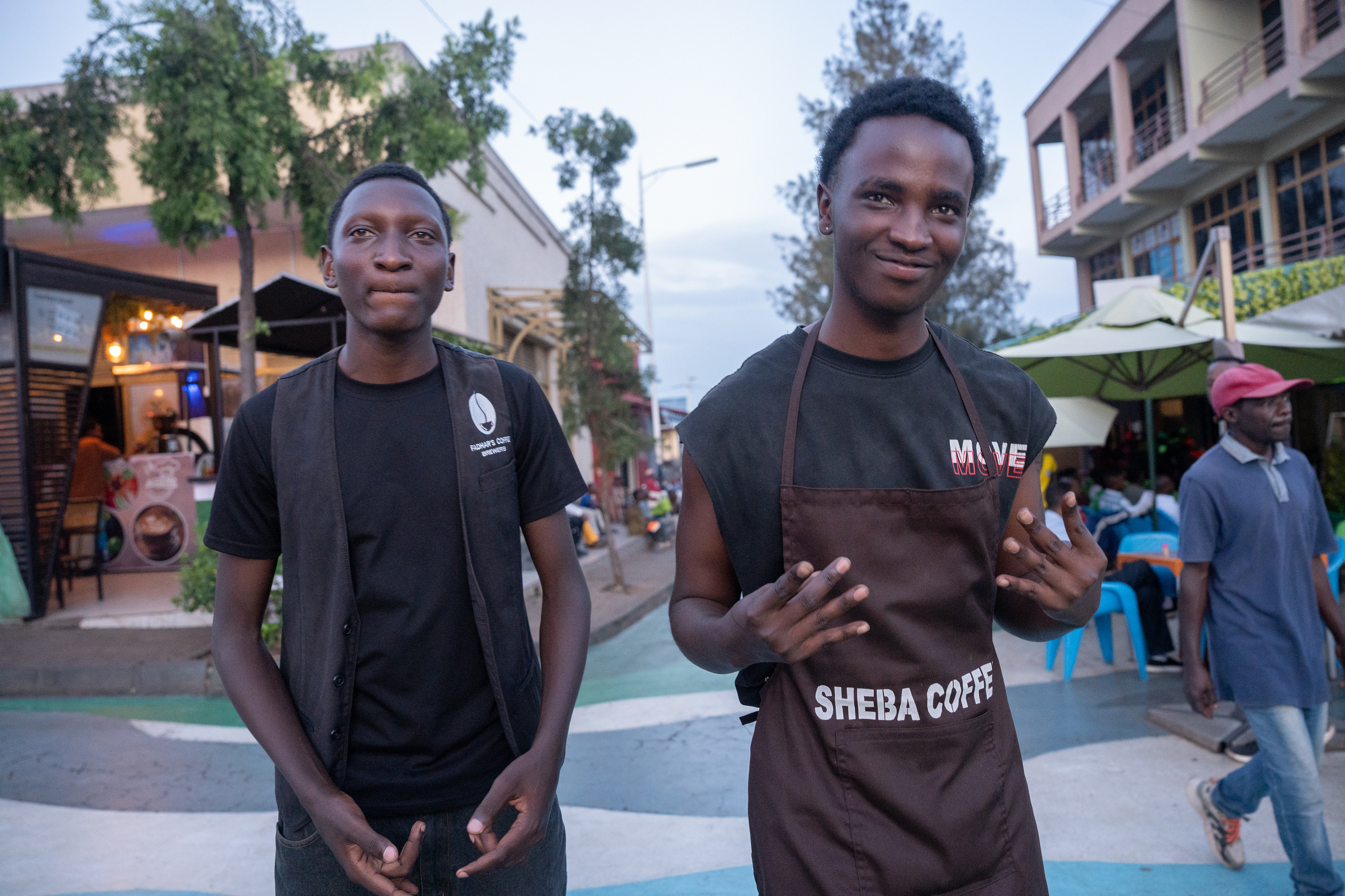 Abdul, left, and Pacifique prepare for a photo while people watch a Premier League football match under the umbrellas in the background on Sunday, May 17, 2026 in Kigali, Rwanda.   Abdul is a fan of Real Madrid and his favorite player is Cristiano Ronaldo, while Pacifique supports Madrid’s rival Barcelona and believes Messi is the greatest player of all time ahead of Ronaldo.   The debate between Messi and Ronaldo comes up often in Rwanda, where football is one of the most popular sports to watch and play.   Rwanda’s official tourism arm, Visit Rwanda, has become one of the most recognizable sponsors in European football through Visit Rwanda’s jersey deals with leading clubs including Paris-Saint Germain in France and Arsenal in England.   Many Rwandans support those teams as a result, which made for an engaging Champions League final between PSG and Arsenal in May.  (Photo/Evan Frilingos 2026)