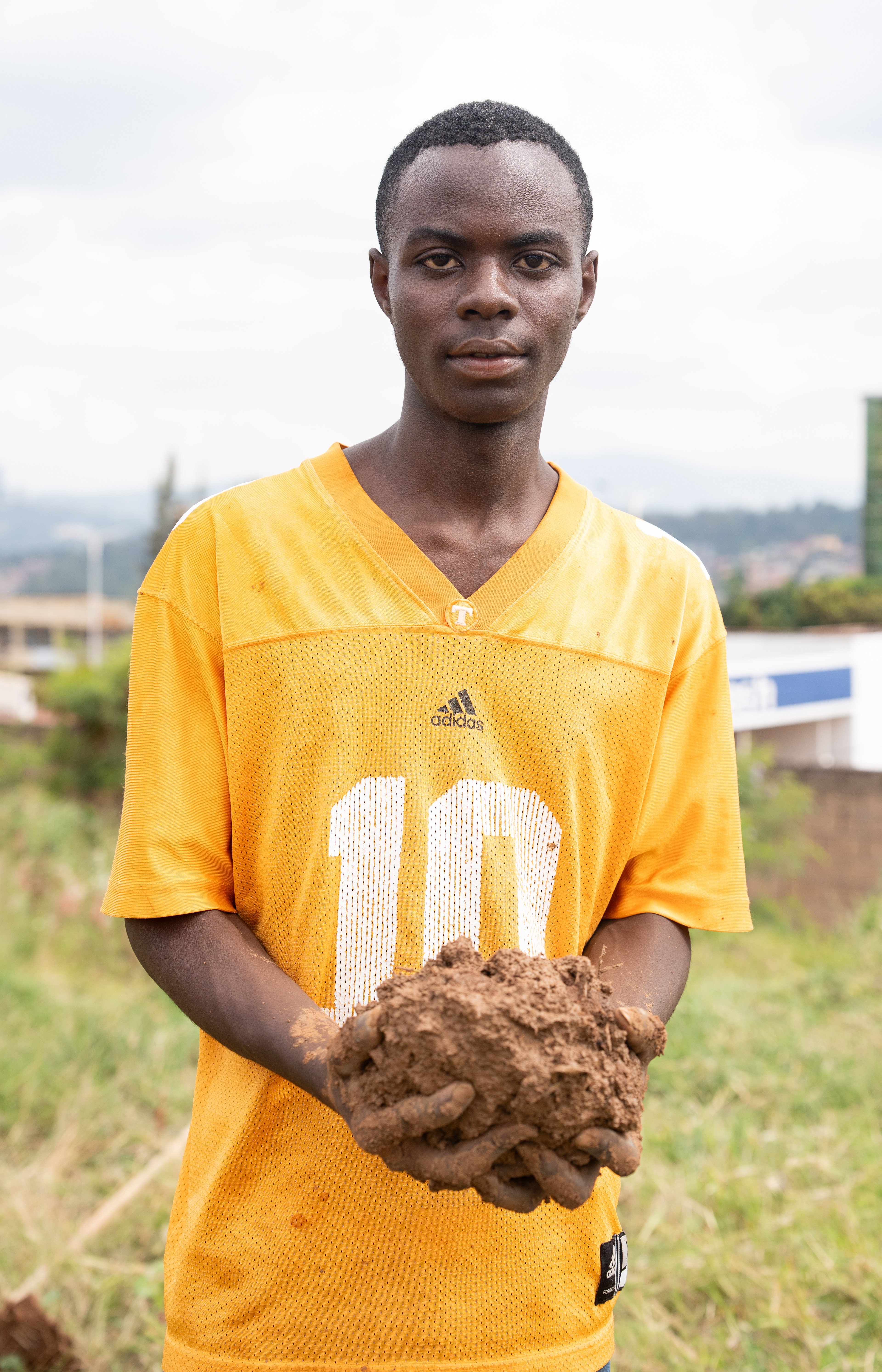 Elissa holds mud before placing it in a brick mold during Umuganda. The bricks would contribute to a new home for orphans in Kigali.   That day Elissa said he traveled over two hours to partake in Umuganda and do a confession at church, and he was one of a large group of young people making mud and bricks.    He said Umuganda was an activity he is proud to take part in and that it is not just a requirement but a part of Rwandan culture, as Paul Kagame also participates in the monthly day of community service.  Service is a way many young people are able to give back to their communities and the people around them.   (Photo/Evan Frilingos 2026)