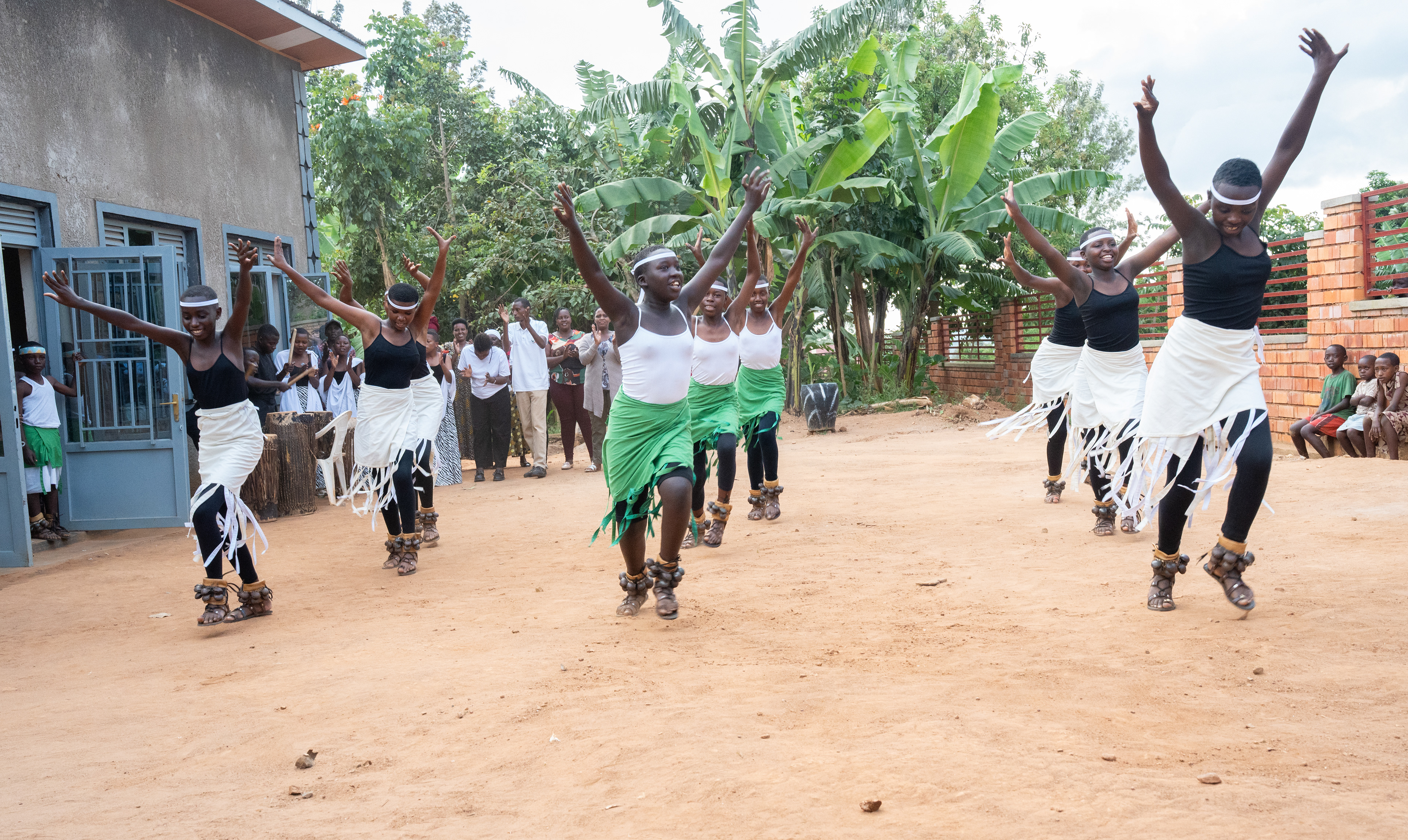 Children from the Unity Mountain, Umusozi w'Ubumwe, community dance across a dirt field while drums, claps and cheers pour out from a group behind them.   The village includes survivors and perpetrators of the 1994 Genocide against the Tutsi who share faith as common ground for reconciliation, forgiveness and unity.   Children running around, peering through fences and holding near to their mothers created a lively, enveloping atmosphere.  (Photo/Evan Frilingos 2026)